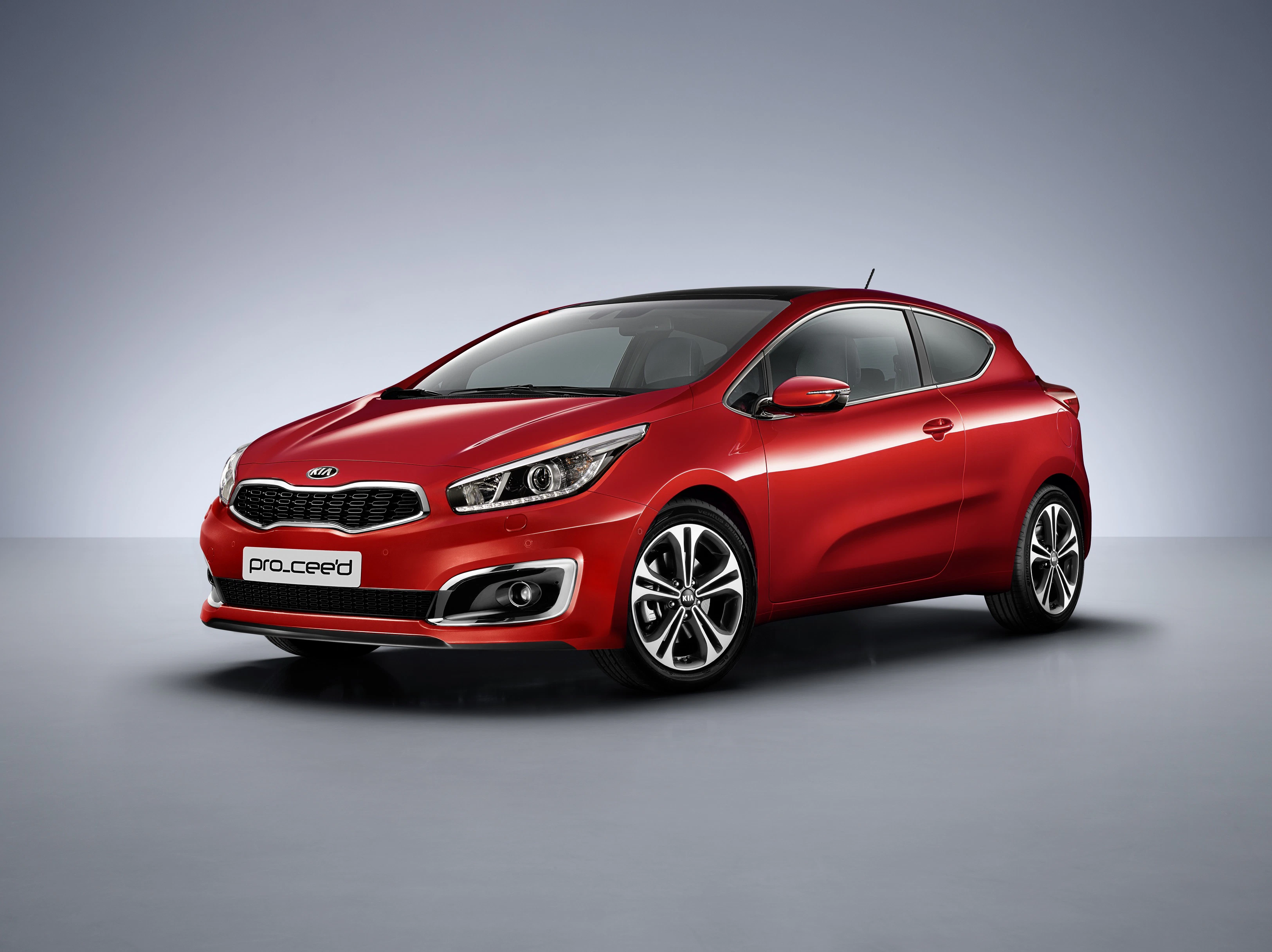 Roter Kia Pro_Cee'd vor grauem Hintergrund, schräg von vorne fotografiert. Dreitüriges Kompaktauto mit modernen Scheinwerfern und Alufelgen.