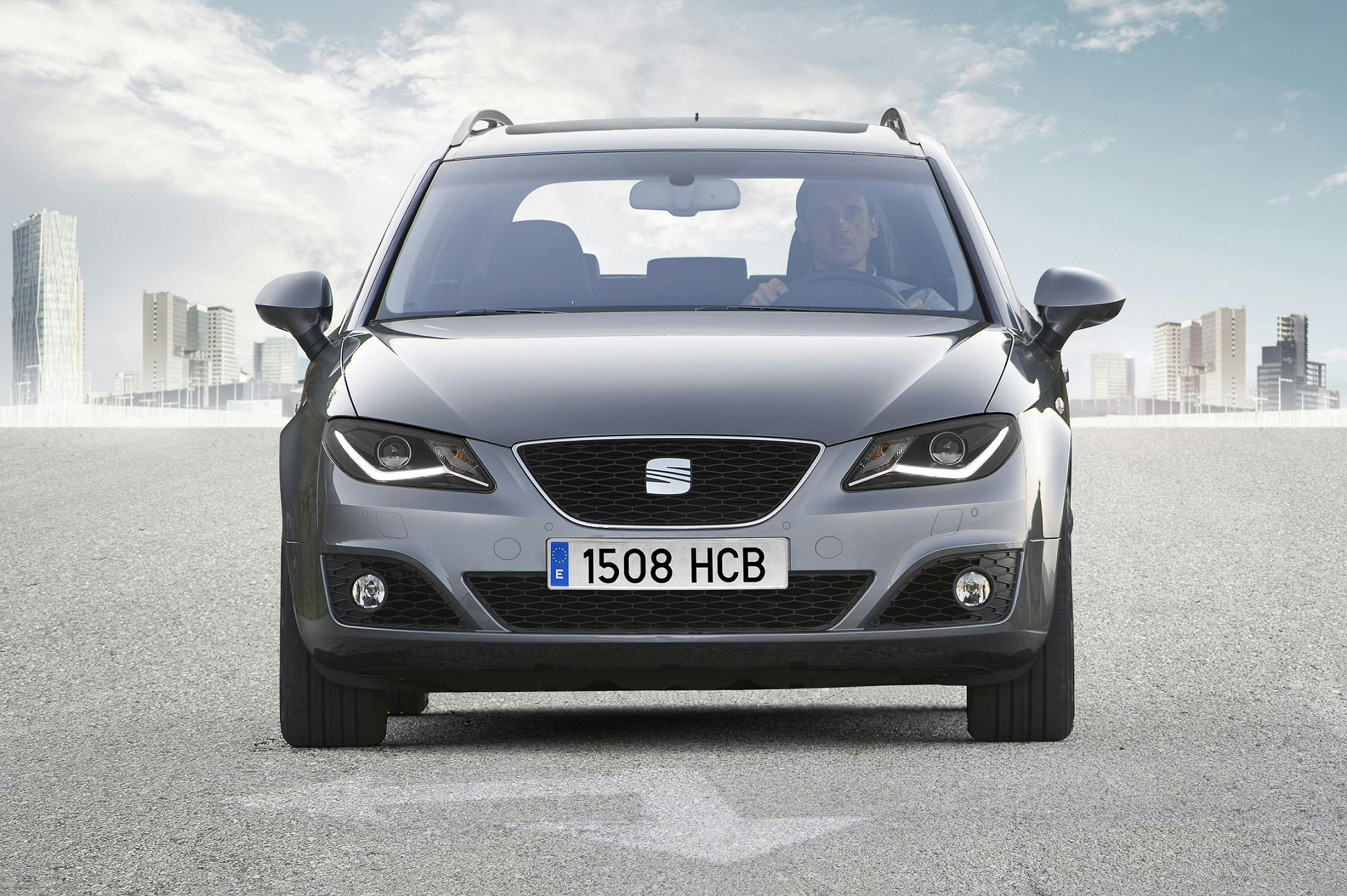 Silberner Kombi auf einer leeren Straße mit Stadtansicht im Hintergrund. Person am Steuer, Nummernschild „1508 HCB“.