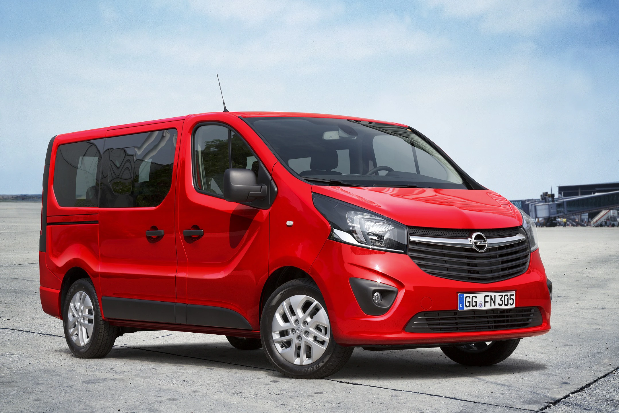 Roter Opel-Vivaro-Kleinbus auf Betonfläche; moderne Karosserie, fünf Türen, glänzende Lackierung, umrissene Radkästen.