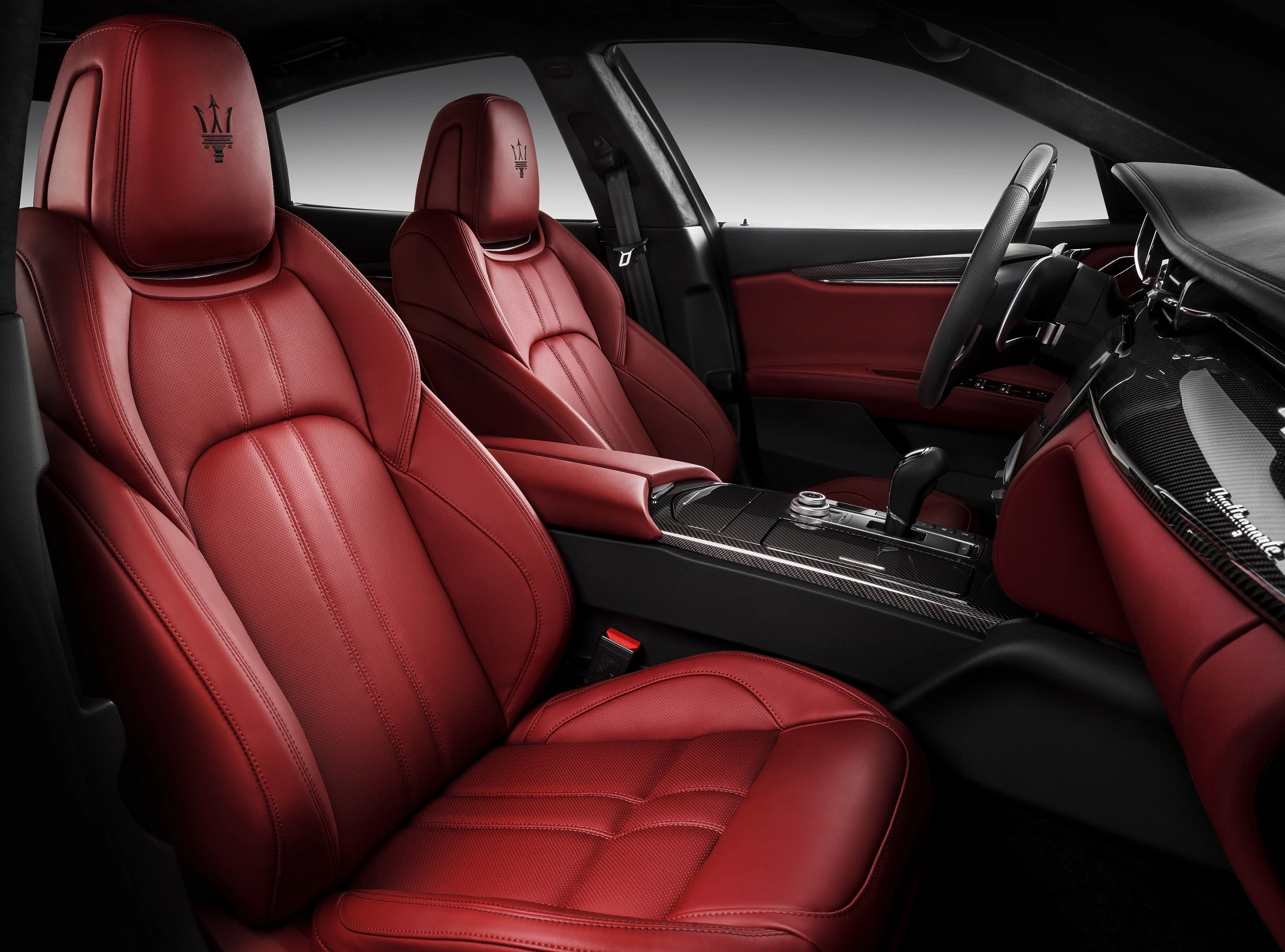 Innenansicht eines Autos mit roten Ledersitzen, elegantem Armaturenbrett und Mittelkonsole mit Schaltknüppel und modernen Kontrollen.