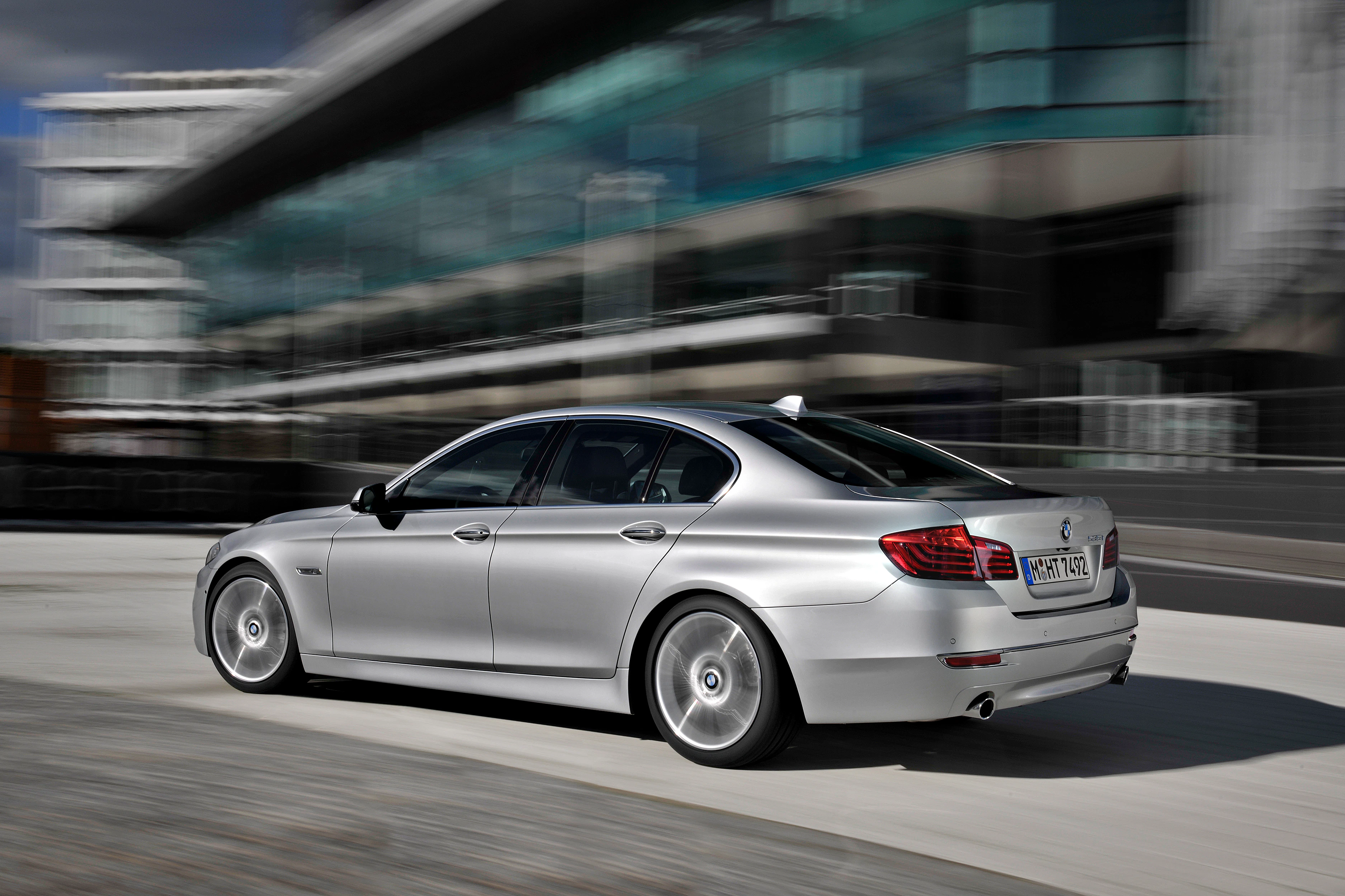 Silberner BMW-Limousine fährt dynamisch auf einer Stadtautobahn vor einer modernen Gebäude.