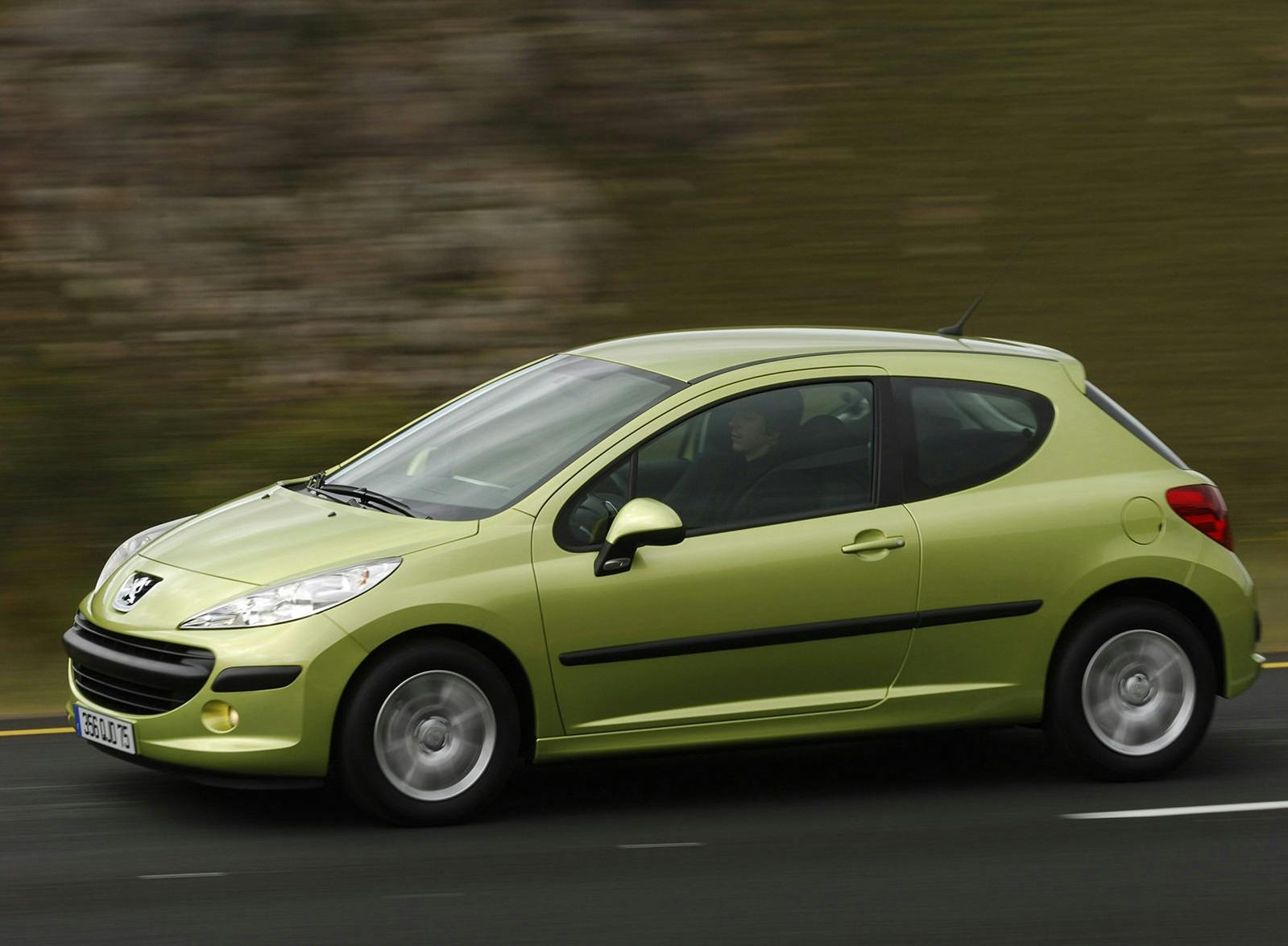Grünes Auto, Peugeot, in Bewegung auf einer Landstraße. Seitenansicht, verschwommener Hintergrund, dynamische Darstellung der Fahrt.