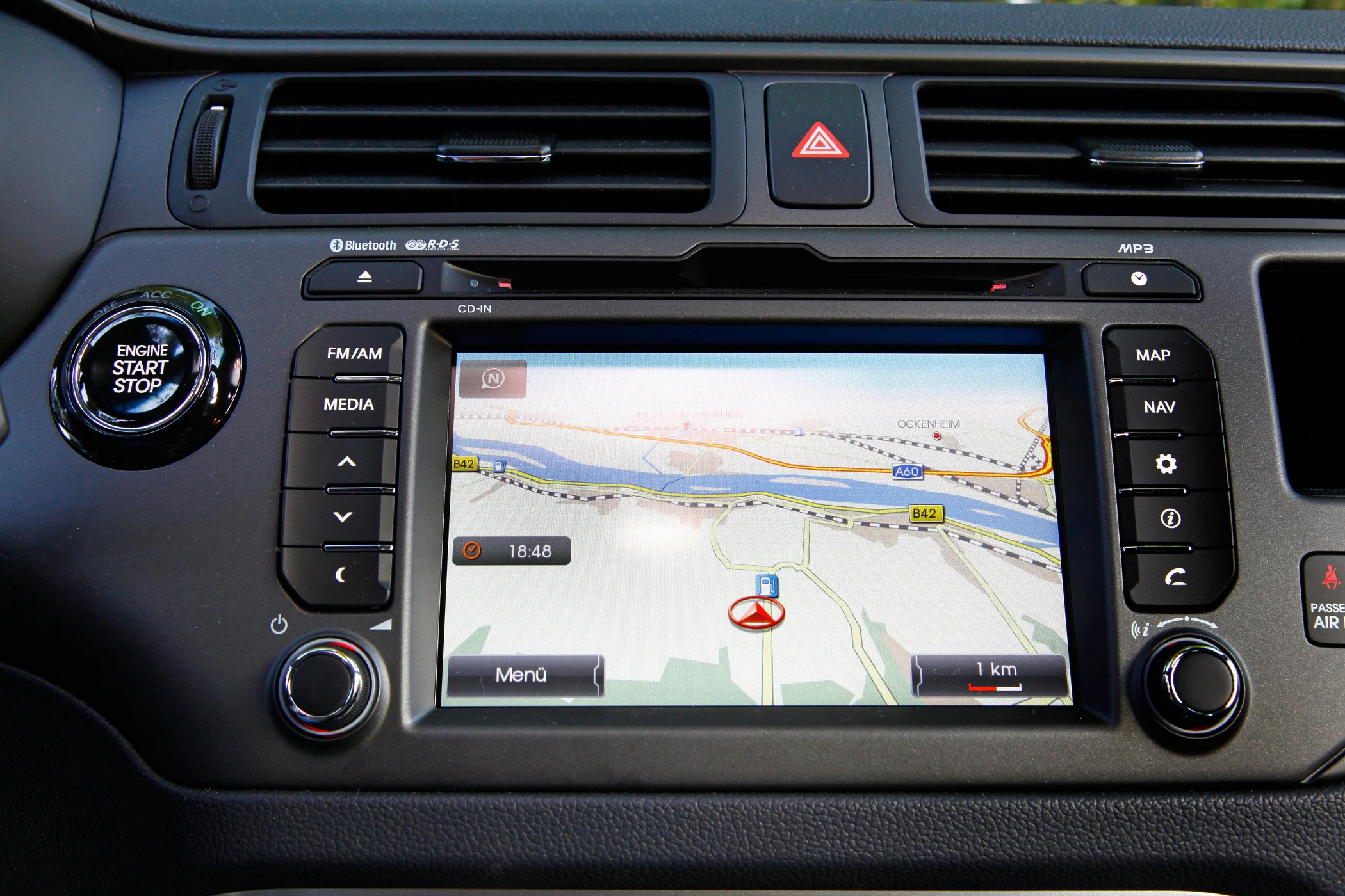Navigationssystem in einem Auto zeigt eine Straßenkarte mit Route. Knöpfe umgeben den Bildschirm, darunter Start, Media und Menü.