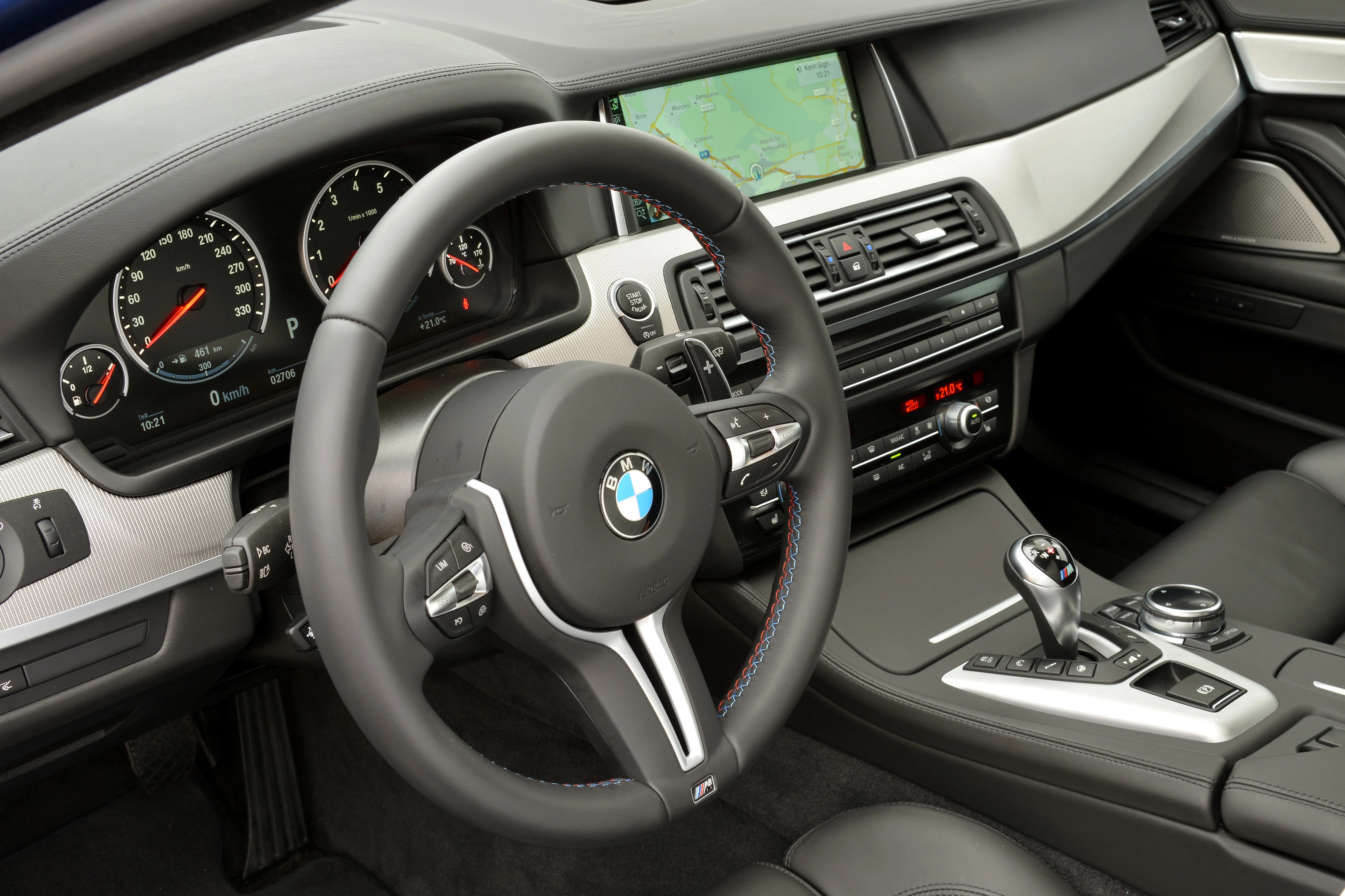 Innenraum eines BMW mit Multifunktionslenkrad, Armaturenbrett mit digitalen Anzeigen, Gangschaltung und eingebautem Navigationssystem.