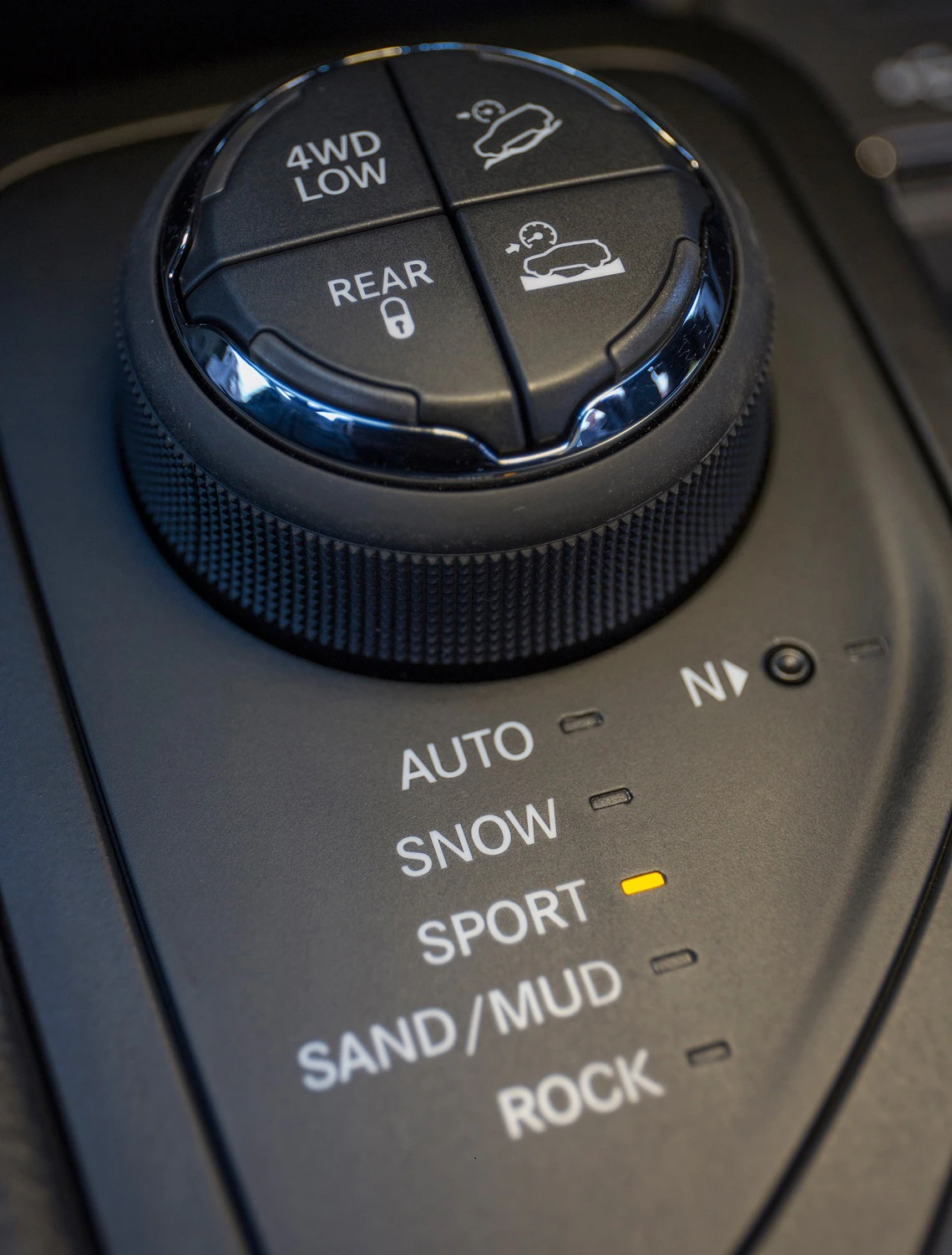 Nahaufnahme eines Fahrzeugkontrollknopfs mit verschiedenen Fahrmodi: Auto, Snow, Sport, Sand/Mud, Rock und 4WD Low.