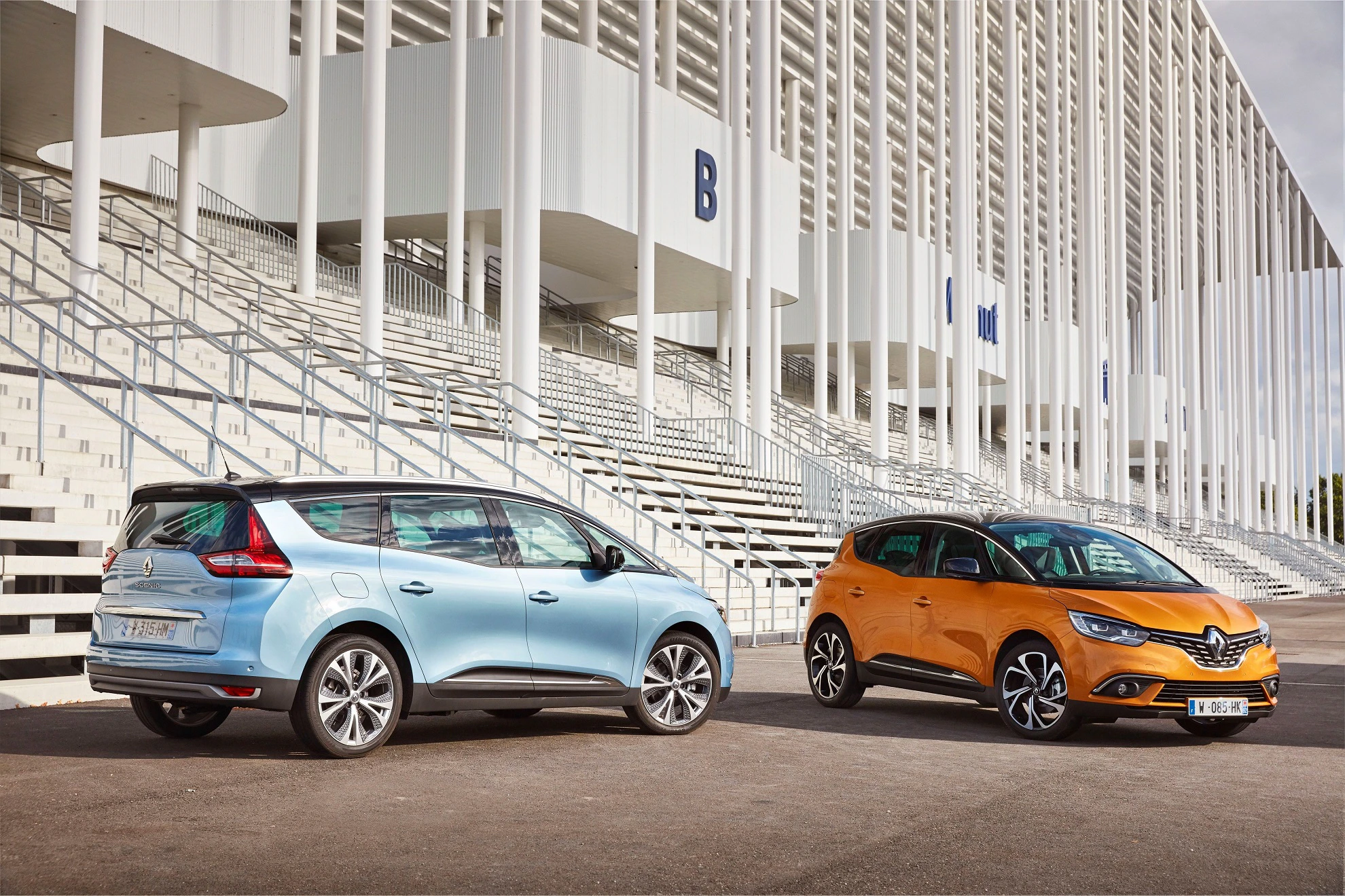 Zwei Renault-Fahrzeuge, ein blauer und ein orangefarbener, stehen vor einem modernen Gebäude mit weißer Fassade und Treppen.