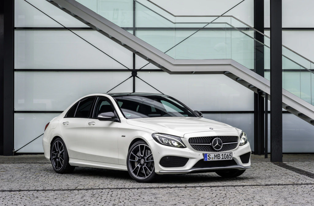 Weiße Mercedes-Benz Limousine, seitlich fotografiert vor einer modernen Glasfassade und Treppen, auf gepflastertem Boden stehend.