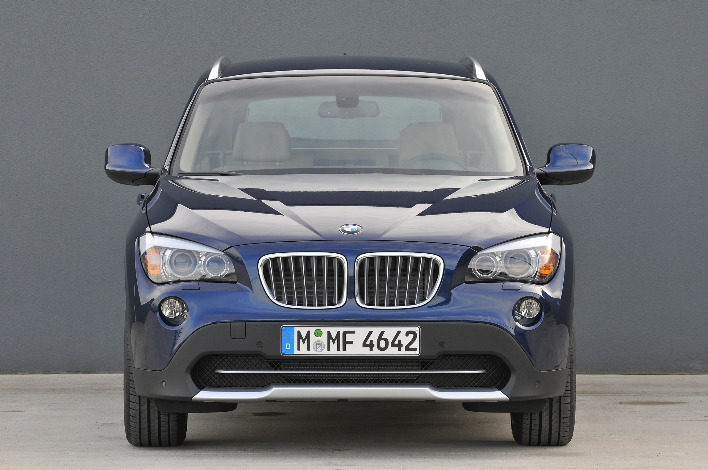 Blauer BMW SUV, Frontansicht, auf grauem Hintergrund geparkt, Kennzeichen mit der Aufschrift "M MF 4642".