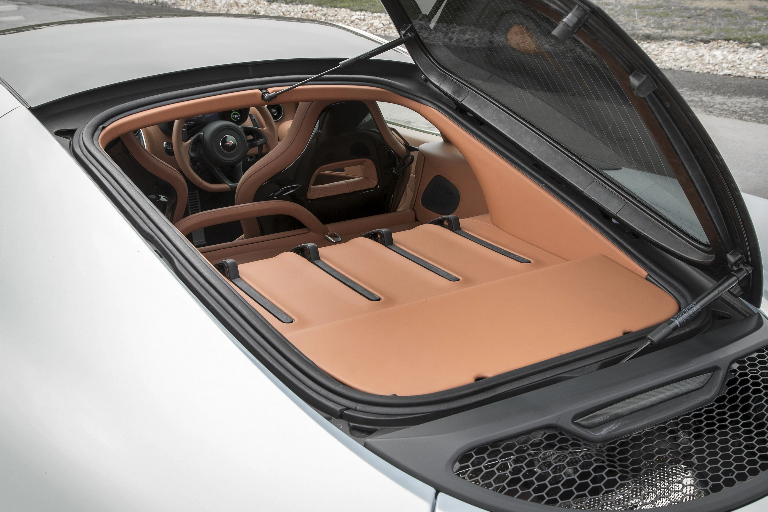 Blick in den Kofferraum eines Sportwagens mit offener Heckklappe, braunem Lederinterieur und Lenkrad sichtbar.