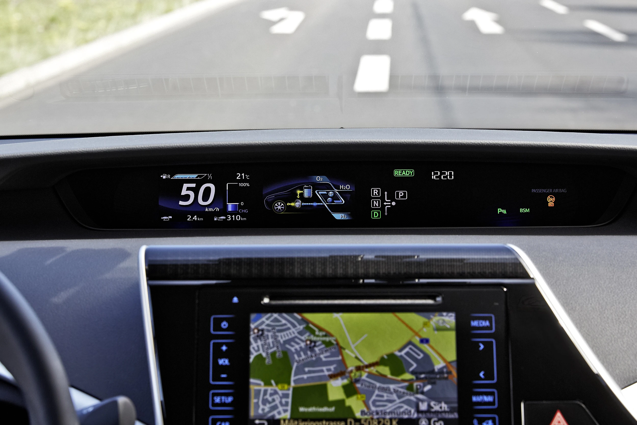 Armaturenbrett eines Autos mit digitalen Anzeigen, darunter Geschwindigkeit, Benzinstand und Navigationssystem auf der Straße.