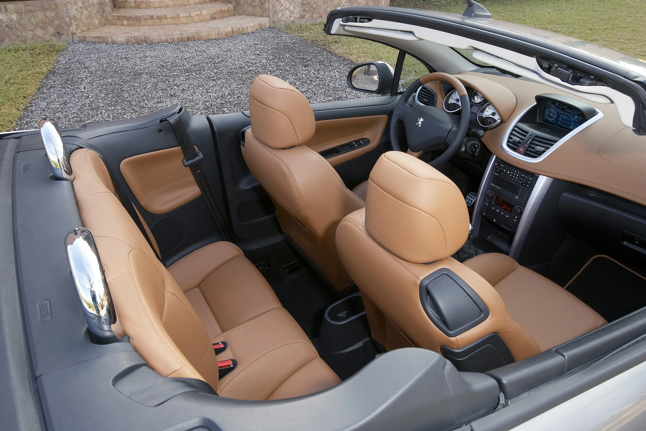 Cabriolet mit beigen Ledersitzen, offenem Dach, modernem Armaturenbrett und lenkradzentriertem Cockpit, steht auf einem Kiesplatz.
