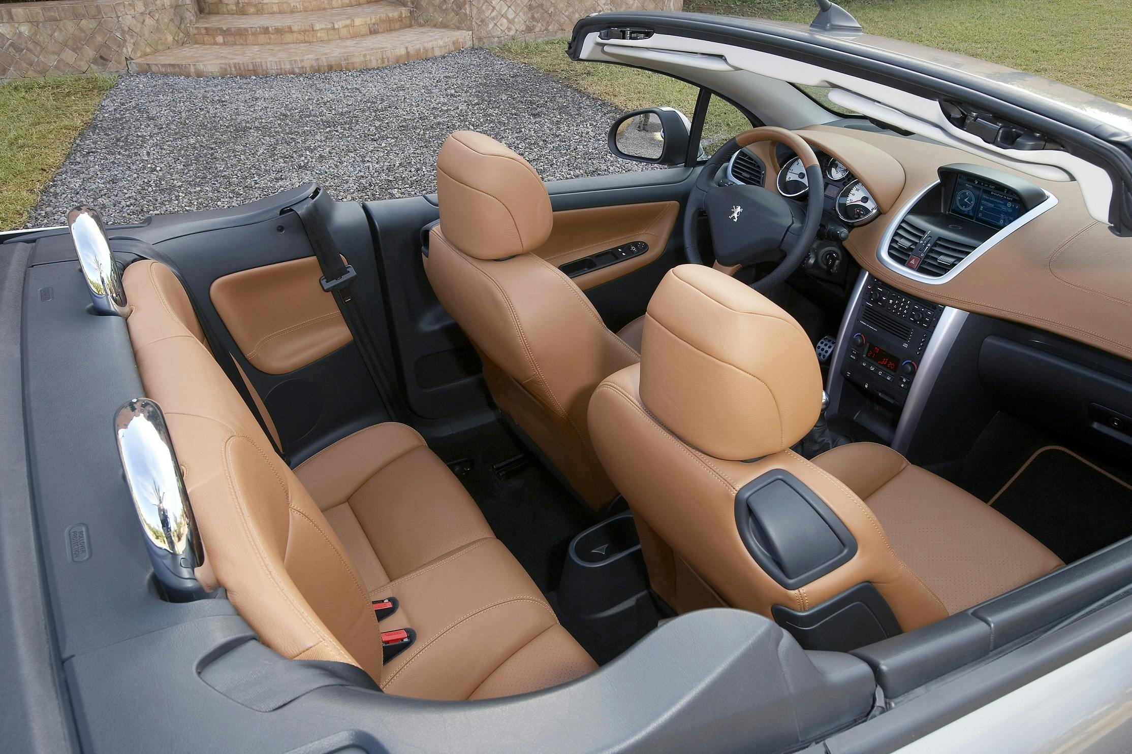 Cabriolet mit beigen Ledersitzen, offenem Dach, modernem Armaturenbrett und lenkradzentriertem Cockpit, steht auf einem Kiesplatz.