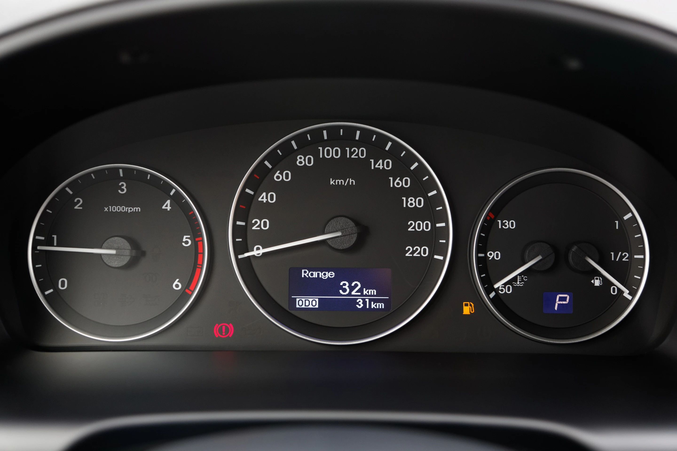 Tachometer eines Autos mit Geschwindigkeitsanzeige, Drehzahlmesser und Tankanzeige. Die Reichweite beträgt 32 km bei niedrigem Kraftstoffstand.
