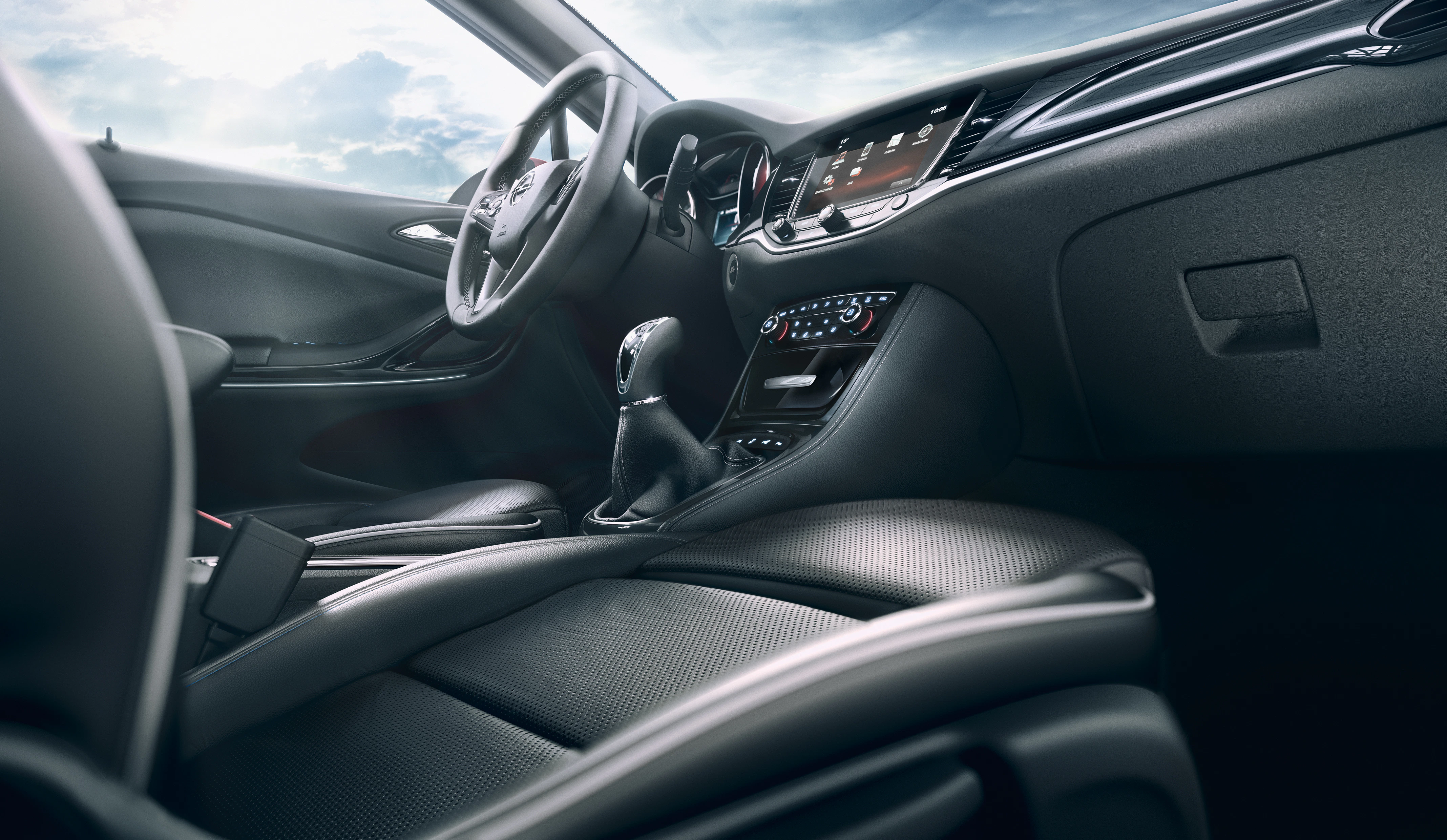 Innenraum eines Autos mit Lenkrad, Schalthebel und Infotainment-System. Lederpolsterung und modernes Design, Blick nach draußen auf Himmel.