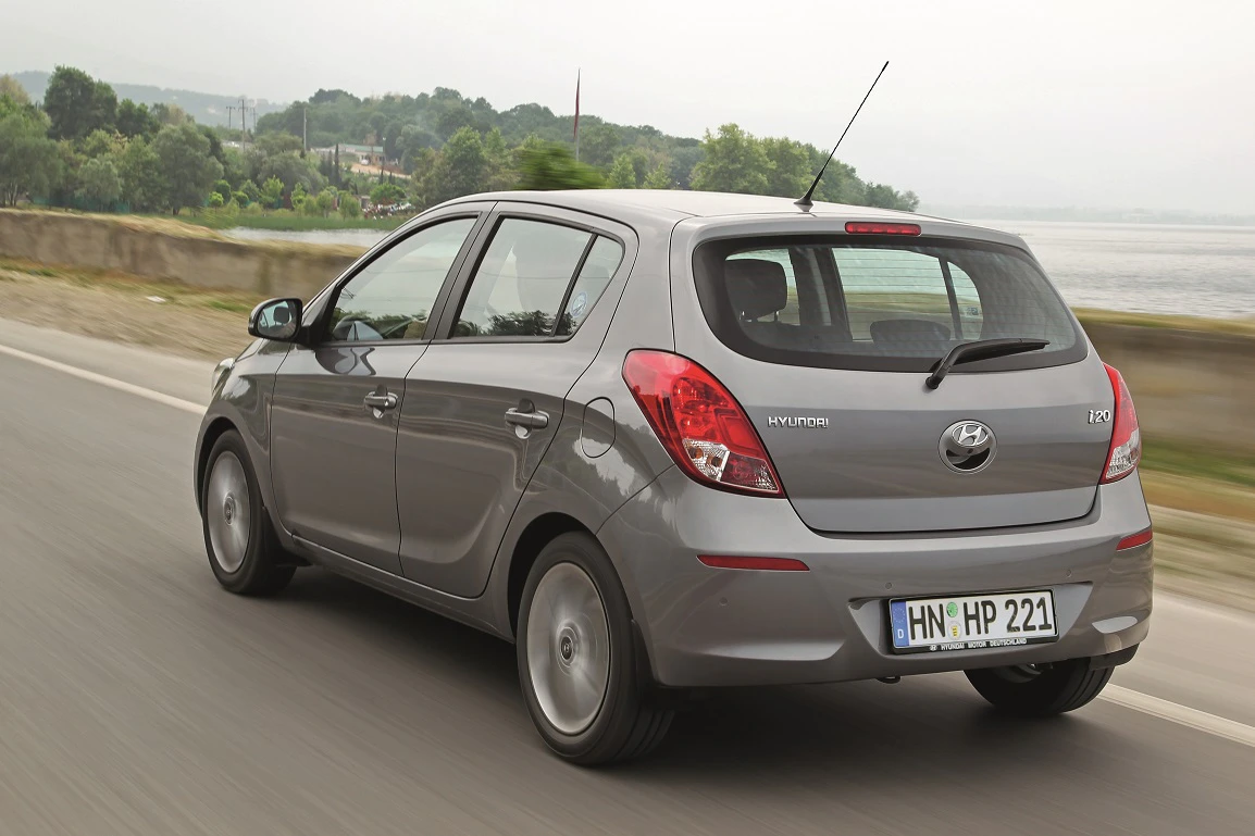 Graues Hyundai i20 Auto fährt auf einer Landstraße entlang eines Flusses, mit Bäumen im Hintergrund an einem bewölkten Tag.
