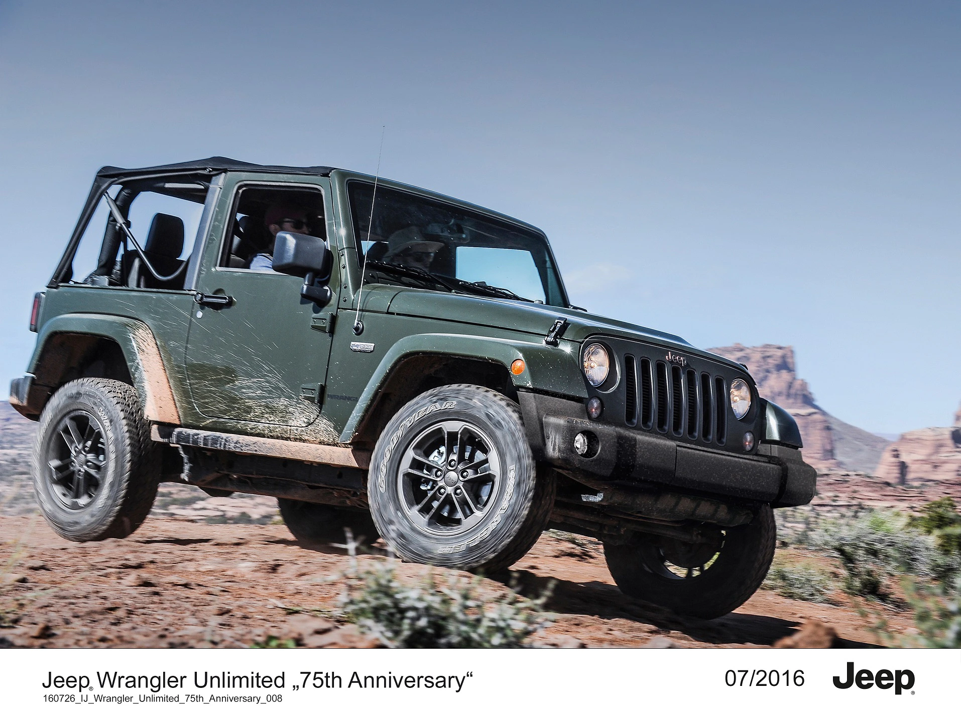 Ein grüner Jeep Wrangler Unlimited fährt im Gelände vor einer Wüstenkulisse mit Felsen. Oben offen, Datum: 07/2016.
