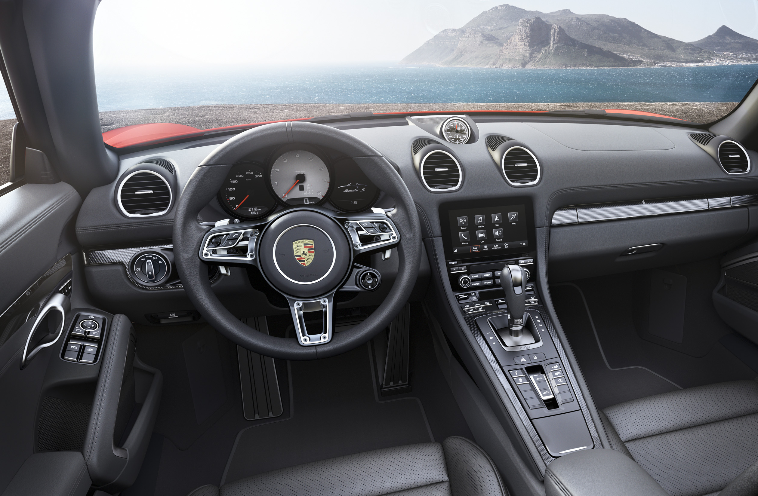 Innenraum eines Porsche mit modernem Armaturenbrett, digitalem Display und sportlichem Lenkrad, mit Blick auf Meer und Berge im Hintergrund.