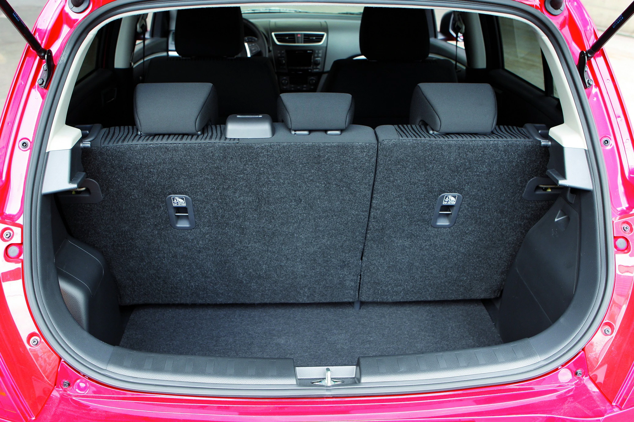 Der Kofferraum eines roten Autos mit umklappbaren Rücksitzen, die hochgeklappt sind. Innenraum in schwarz und grau gehalten.