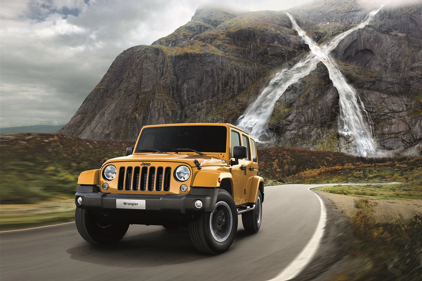 Gelber Jeep Wrangler fährt auf kurviger Straße vor beeindruckender Bergkulisse mit Wasserfällen im Hintergrund.
