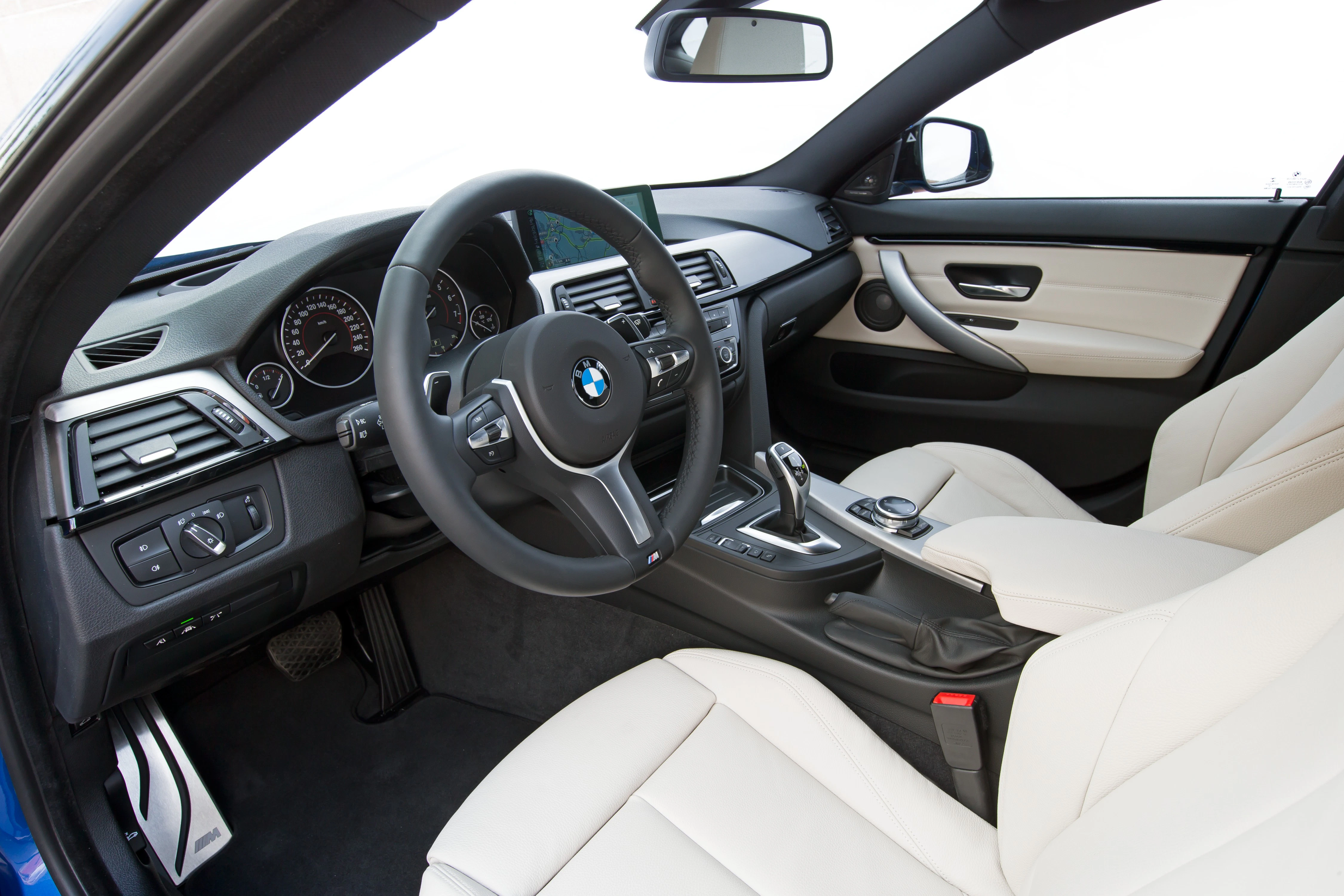 Innenraum eines BMW-Autos mit beigem Leder, modernem Lenkrad, Gangschaltung und Instrumententafel, die ein luxuriöses Ambiente bieten.