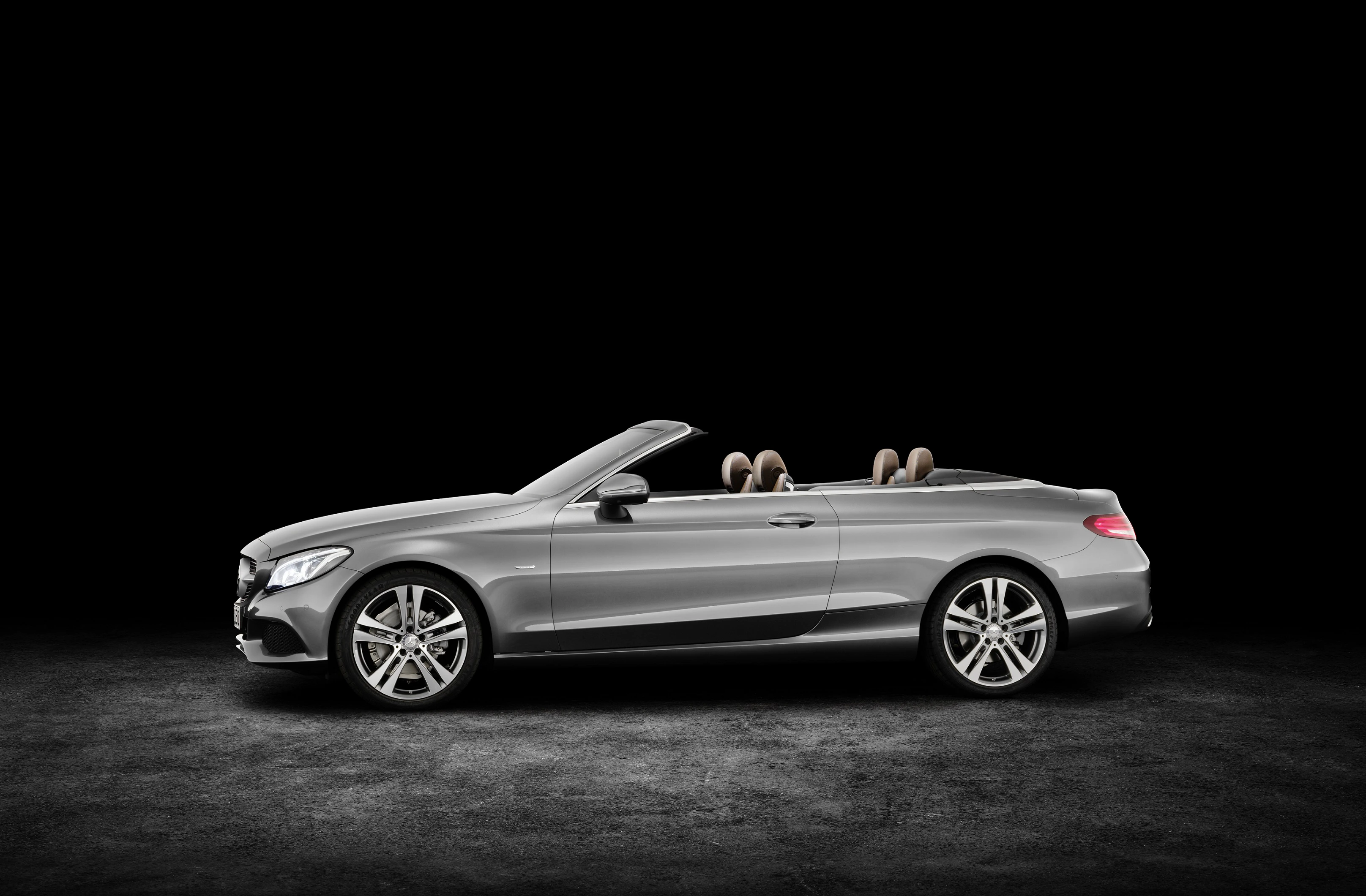 Silbernes Cabriolet, seitlich fotografiert, mit heruntergeklapptem Verdeck, auf dunklem Hintergrund.