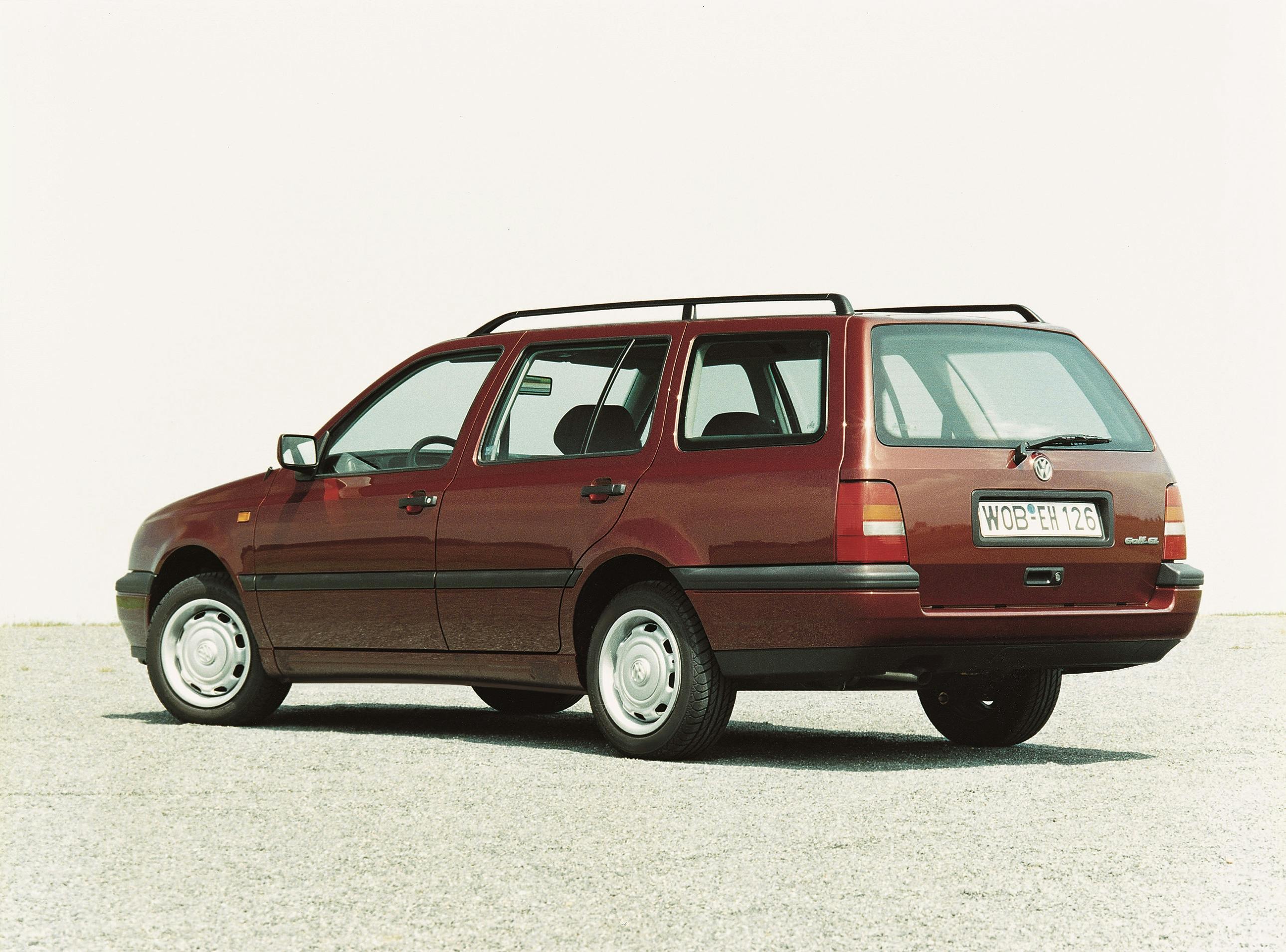 Roter Kombiwagen, älteres Modell, geparkt auf grauem Asphalt vor weißem Hintergrund. Nummernschild sichtbar.