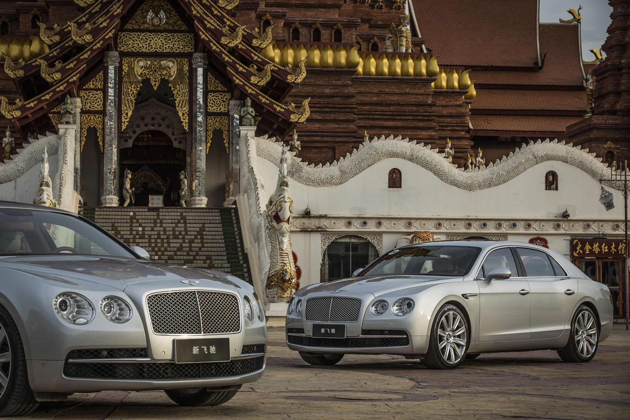 Zwei silberne Luxusautos vor einem imposanten, traditionell verzierten Gebäude mit goldenen Akzenten und geschwungenen Dächern.