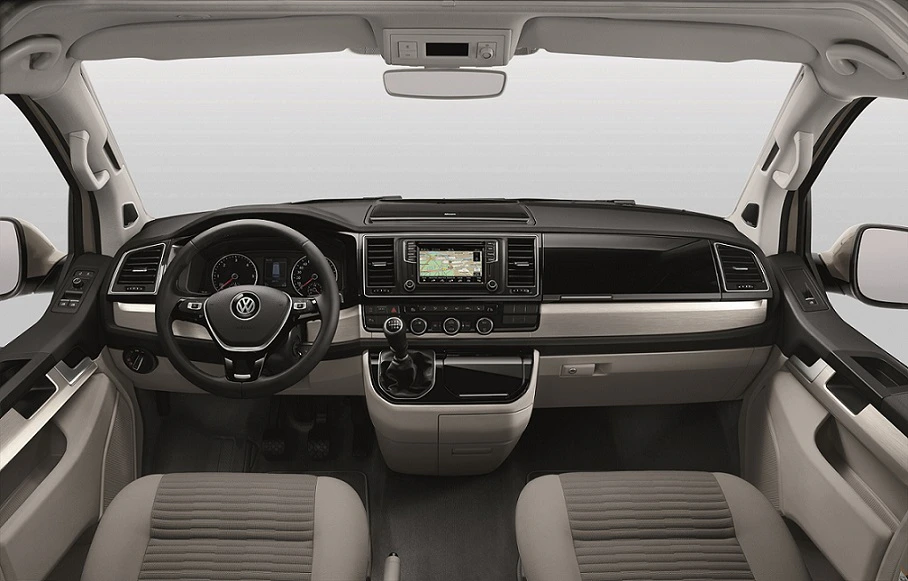 Innenraum eines Volkswagen-Transporters mit modernem Armaturenbrett, Lenkrad, Navigationssystem und Sitzen in Beige- und Grautönen.