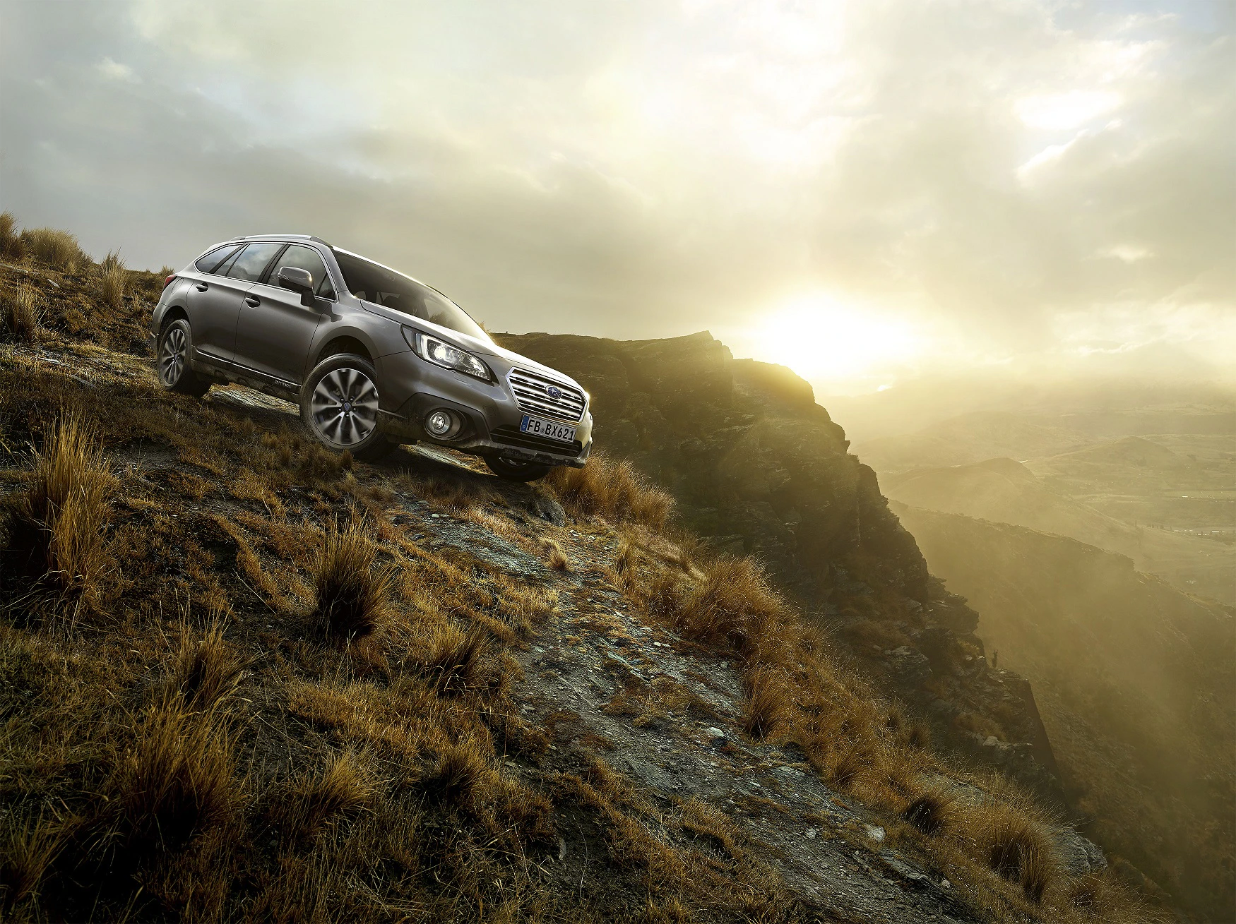 Ein SUV fährt einen steilen, felsigen Hang hinunter bei Sonnenaufgang, umgeben von einer kargen, gebirgigen Landschaft.