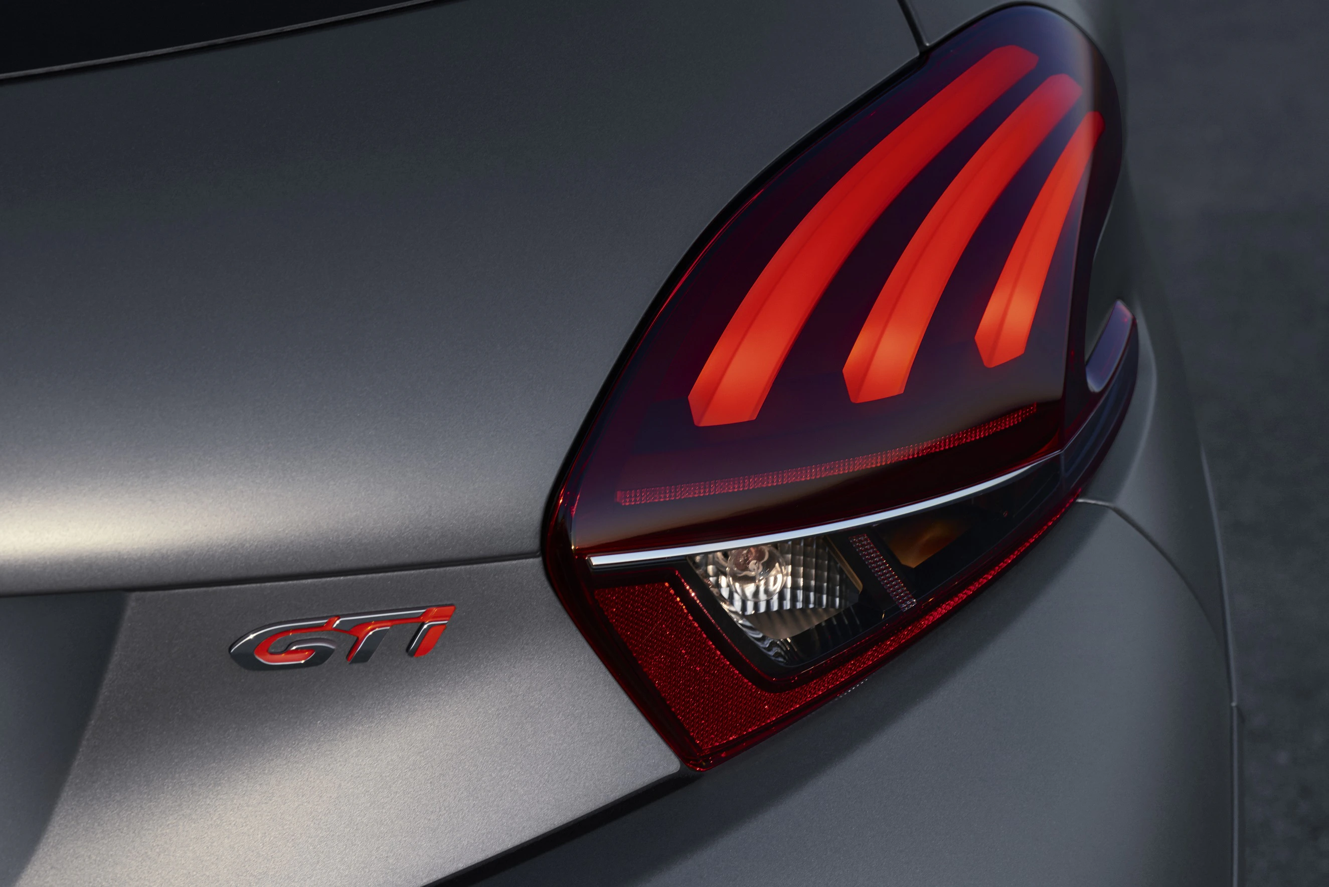 Nahaufnahme eines Autos in Anthrazit, zeigt das Rücklicht mit leuchtenden roten Linien und dem GTI-Logo daneben.