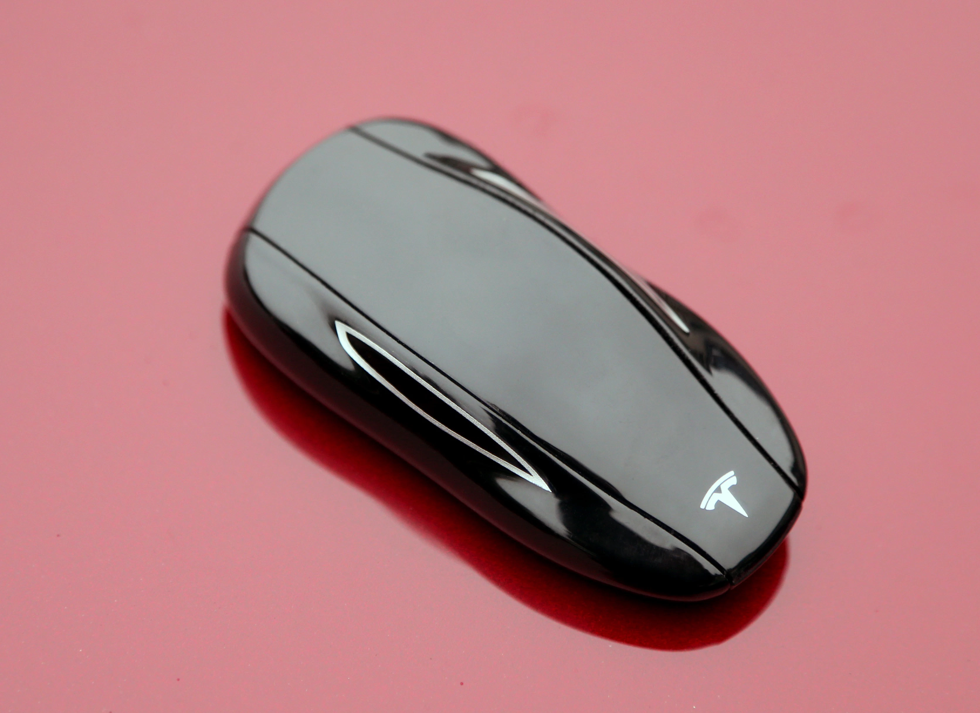 Schwarzer Tesla-Schlüssel in Form eines Autos, auf rotem Hintergrund.