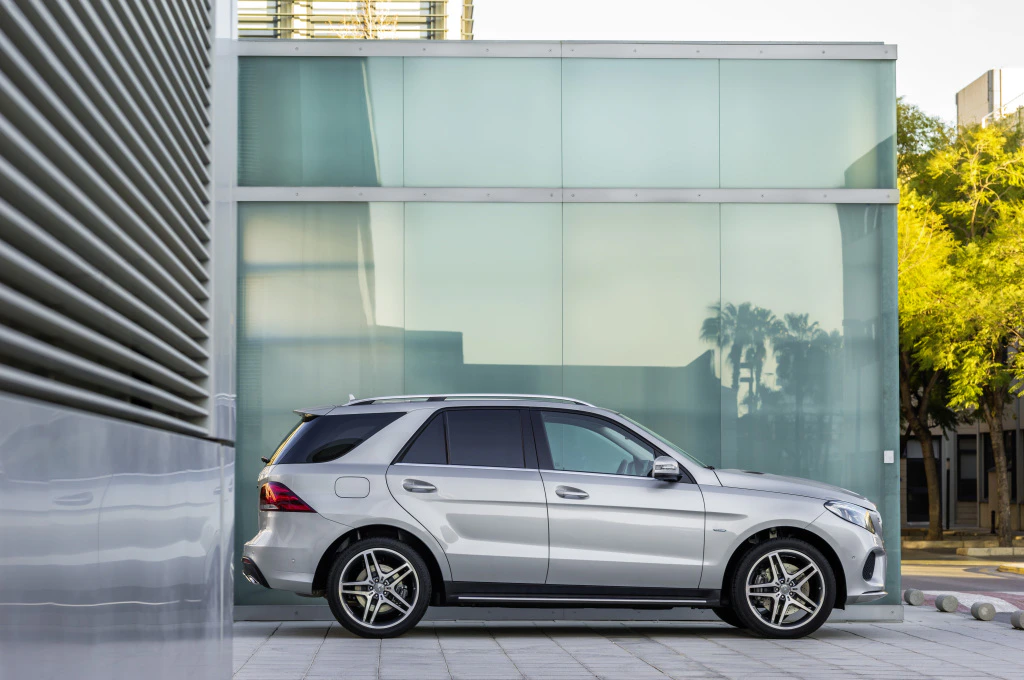 Silberner SUV, seitlich geparkt vor einem modernen Gebäude mit Glasfassade. Im Hintergrund sind Bäume und ein heller Himmel sichtbar.