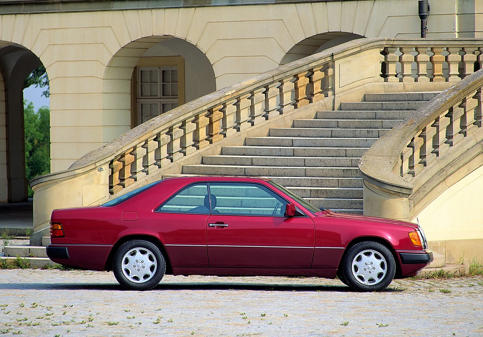 Roter Oldtimer-Coupé vor einem historischen Gebäude mit Steintreppe im Hintergrund.
