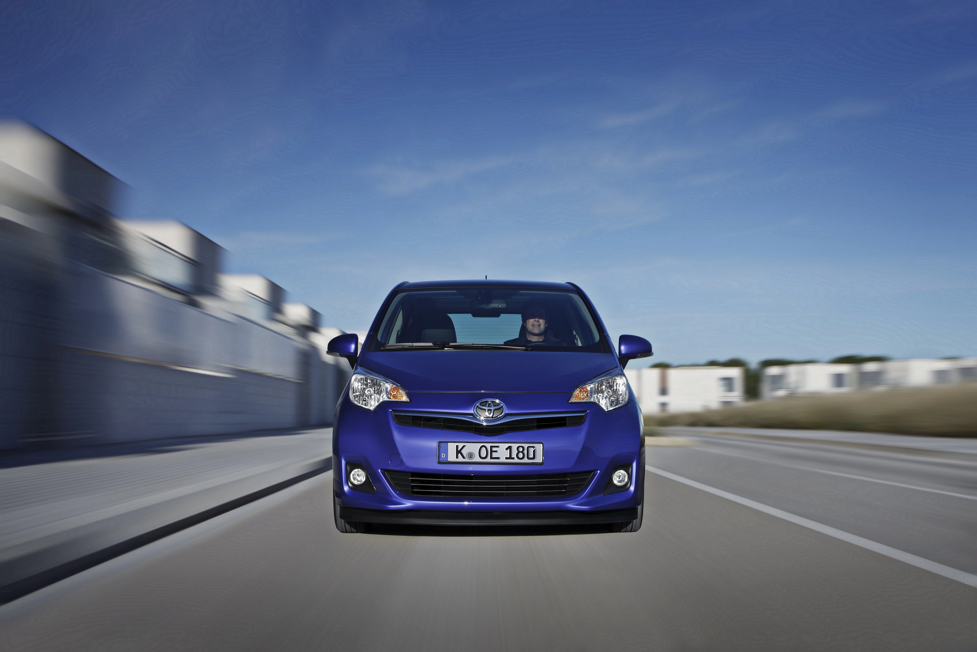 Blauer Toyota Yaris fährt auf einer Stadtstraße mit verschwommenem Hintergrund bei klarem Himmel. Vorderansicht des Autos.