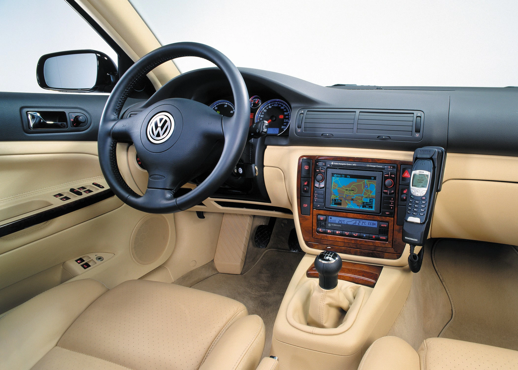 Innenraum eines Volkswagen mit schwarzem Lenkrad, beiger Lederausstattung, Navigationssystem und integriertem Autotelefon.