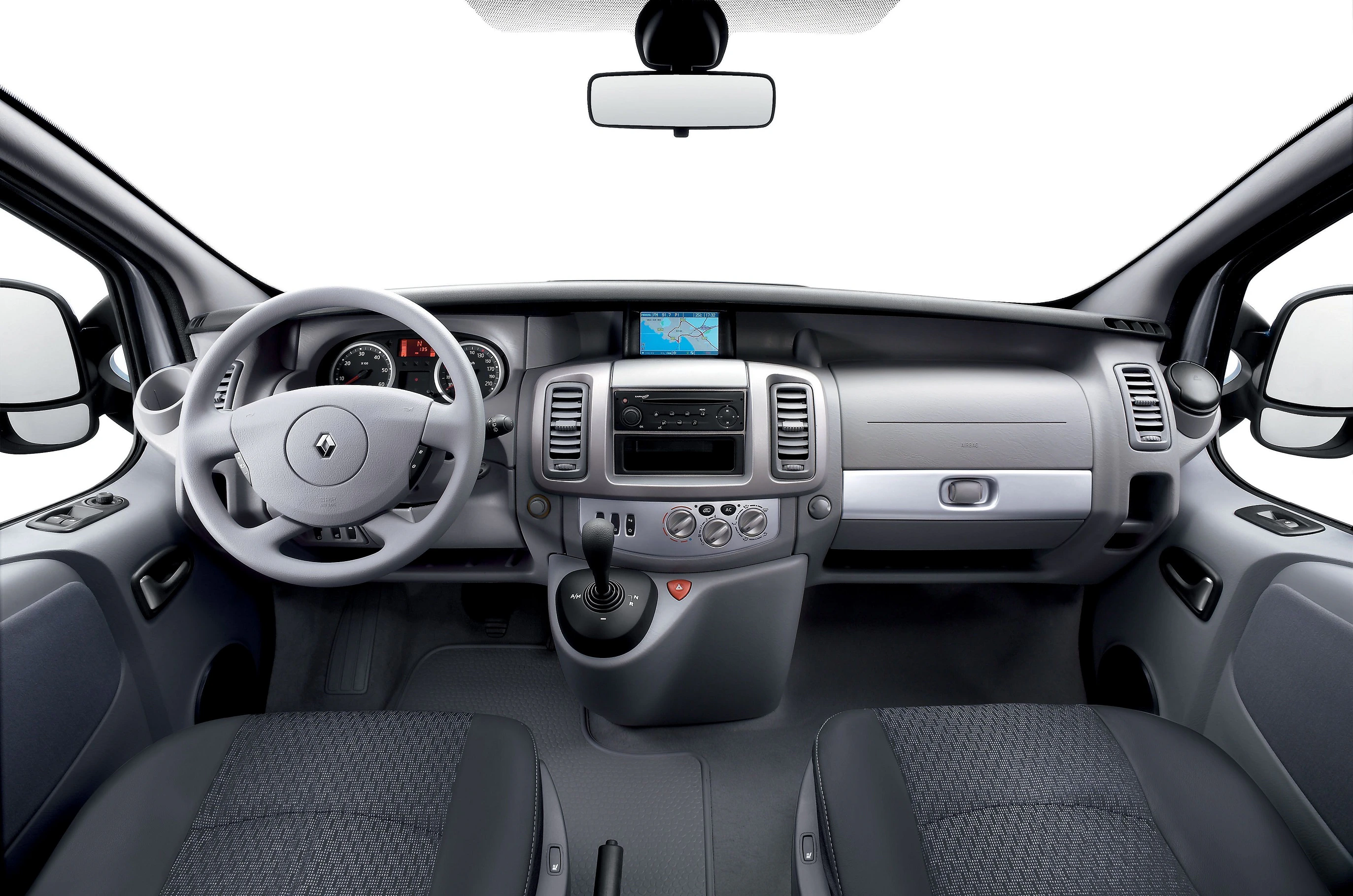 Innenraum eines Fahrzeugs mit grauer Armatur, Lenkrad links, Touchscreen in der Mitte und zwei Vordersitzen.