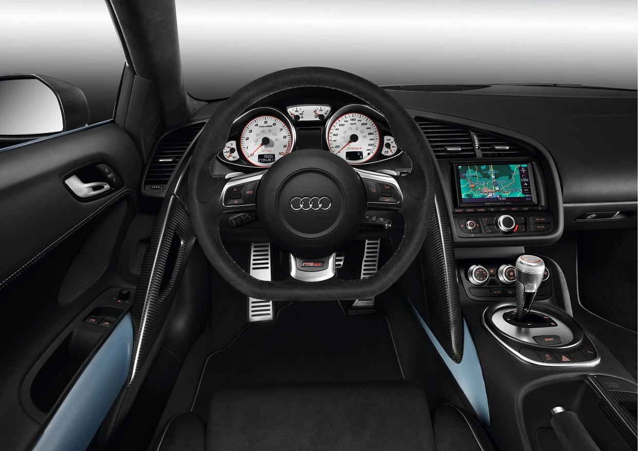 Innenraum eines Autos mit schwarz-weißem Armaturenbrett, Audi-Logo am Lenkrad und Navigationssystem. Sportlicher, luxuriöser Stil.
