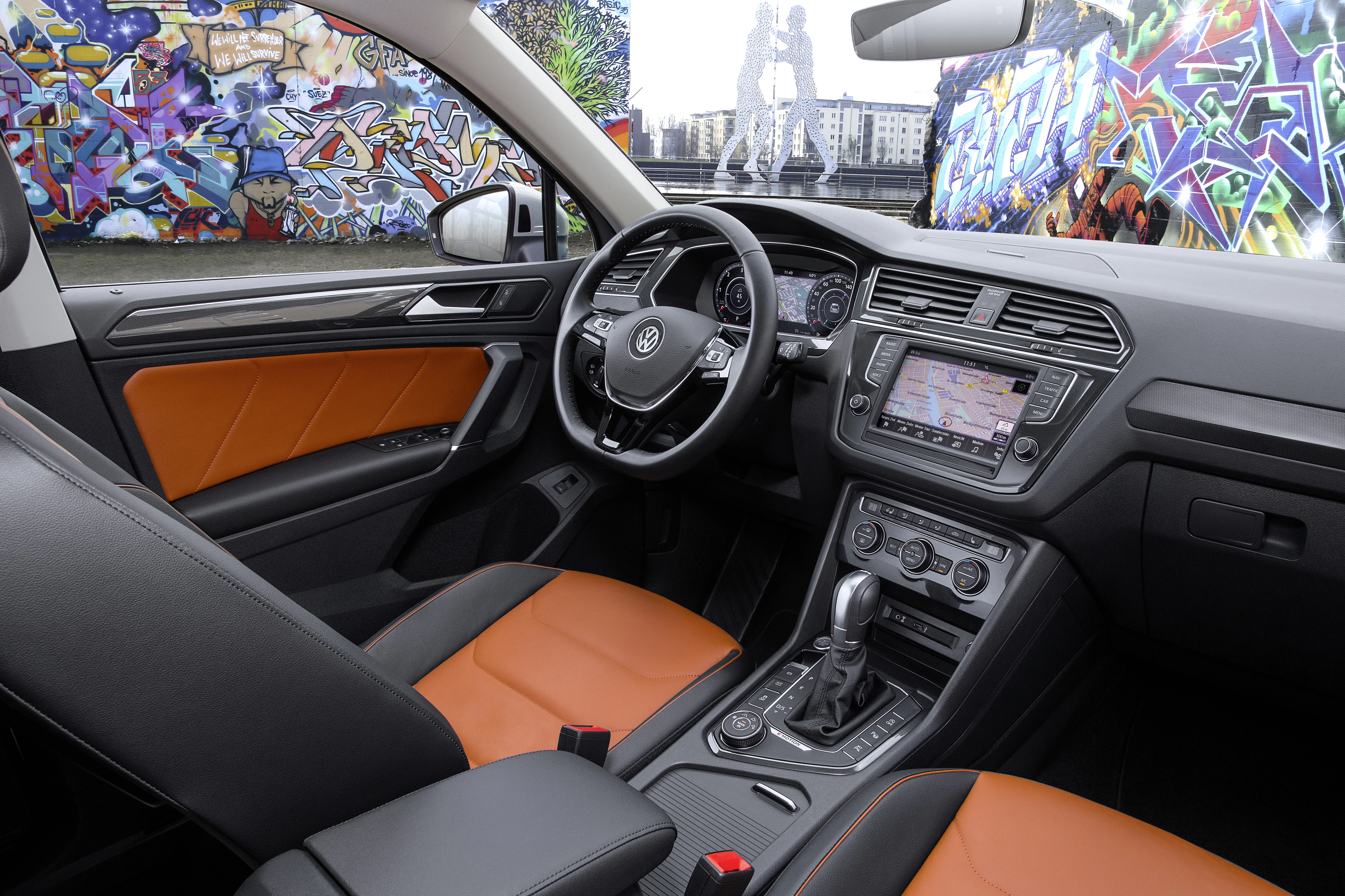 Innenraum eines Autos mit braunen Ledersitzen, modernem Armaturenbrett und Navigation, umgeben von farbenfroher Graffiti-Kunst.