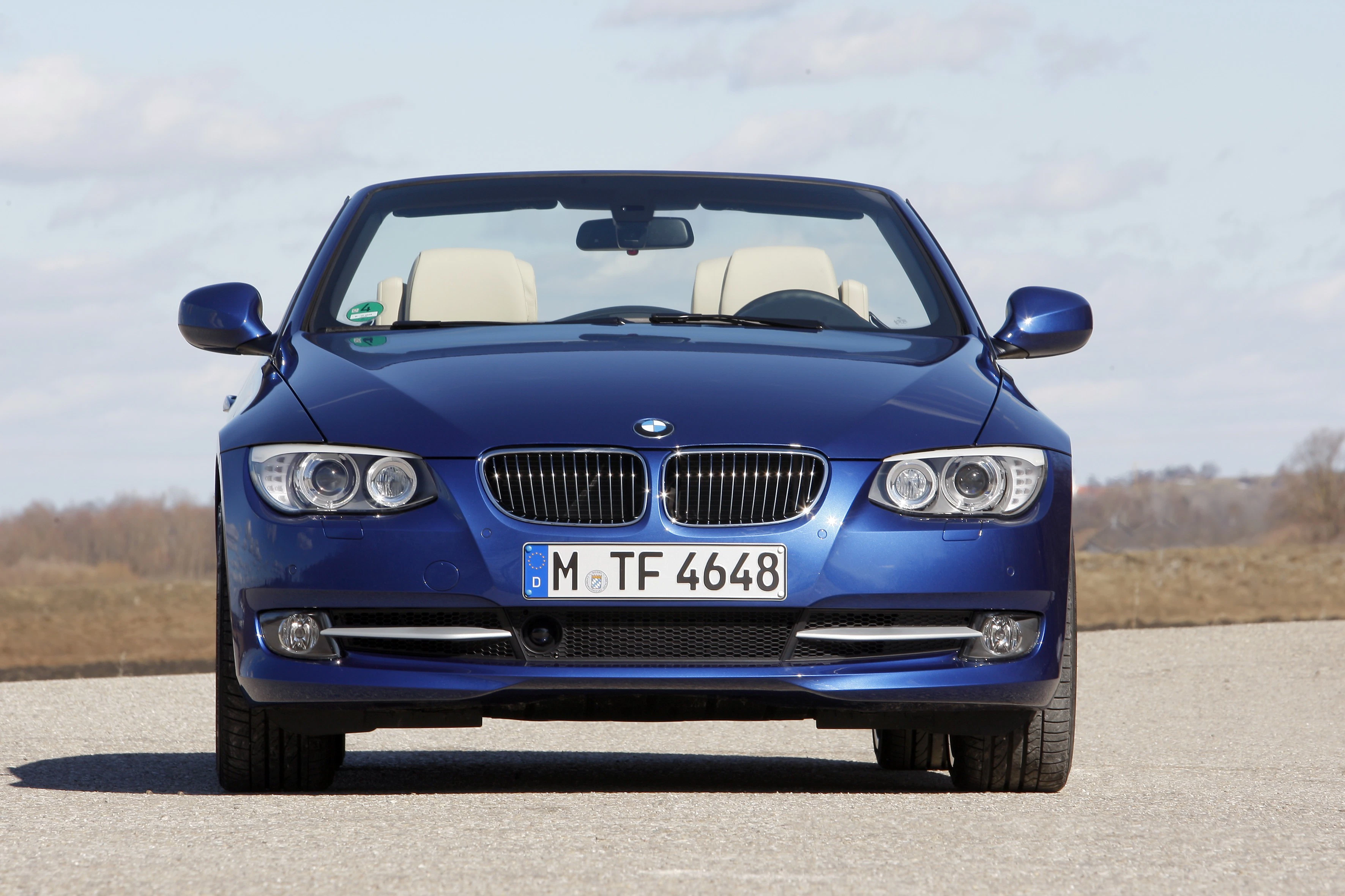 Blaues BMW Cabrio auf einer Straße, frontal fotografiert. Klarer Himmel im Hintergrund.