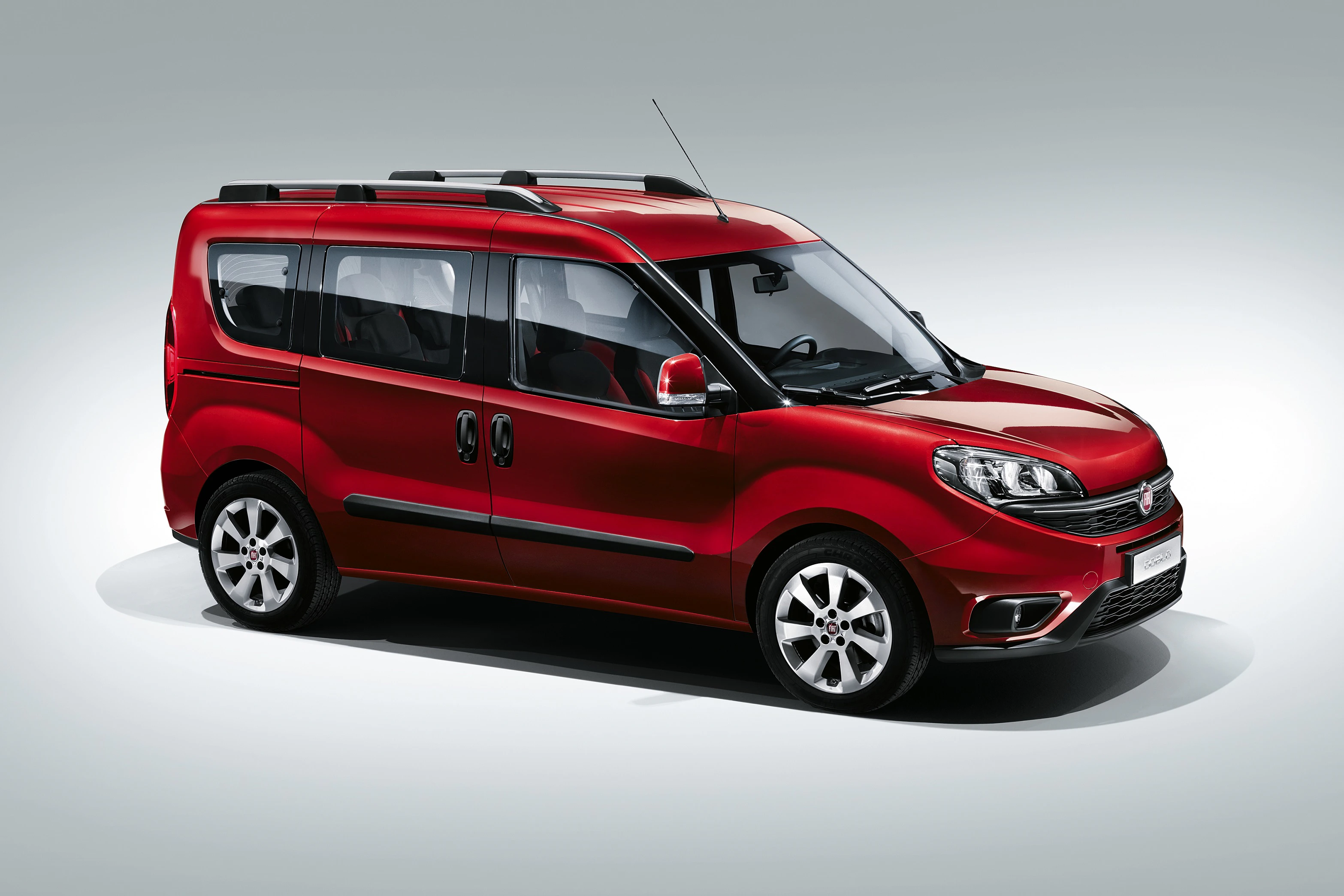 Roter Minivan mit Dachreling, Seiten- und Heckfenstern, steht in einem Studio vor grauem Hintergrund.