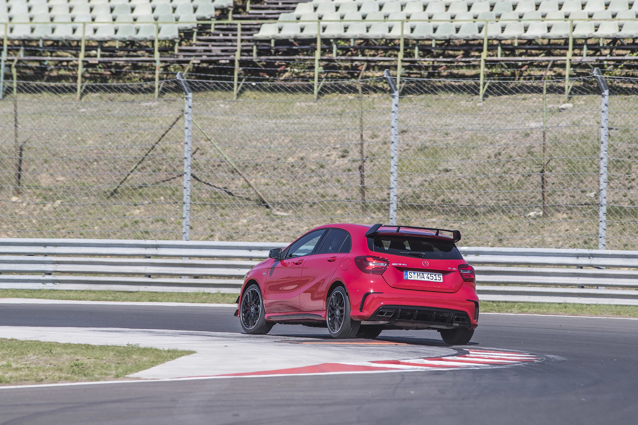 Rotes Auto fährt mit hoher Geschwindigkeit auf einer Rennstrecke. Es hat einen Heckspoiler und sportliches Design. Zuschauertribüne im Hintergrund.