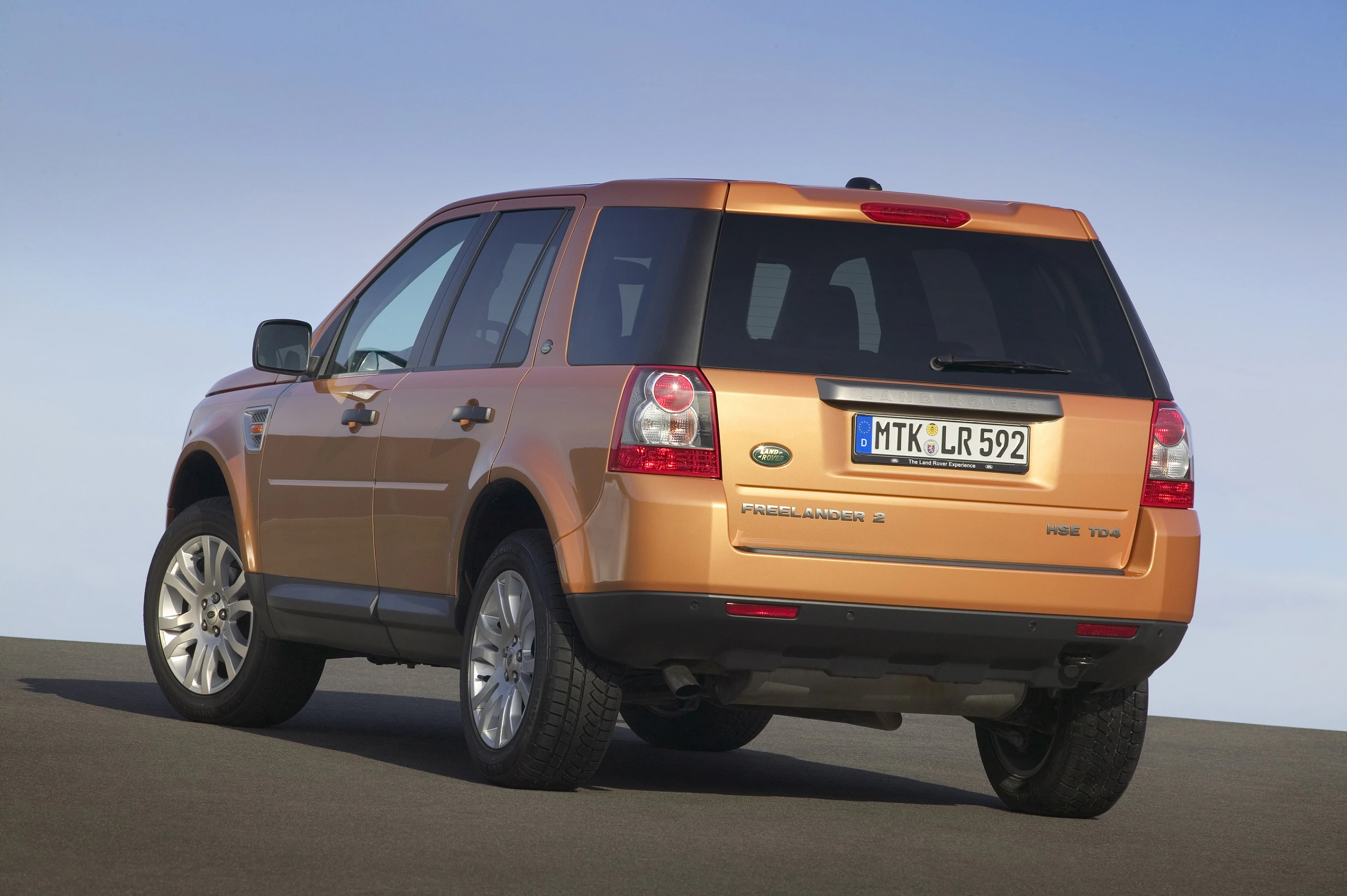 Orangefarbener SUV Land Rover Freelander 2, Heckansicht, parkt auf Asphalt, deutscher Kennzeichen MTK-LR 592 sichtbar.