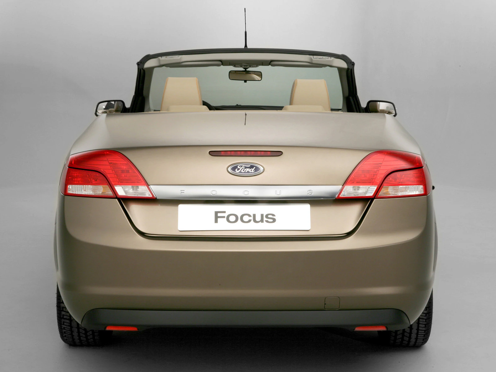 Rückansicht eines goldfarbenen Ford Focus Cabrios mit geöffnetem Verdeck auf grauem Hintergrund.