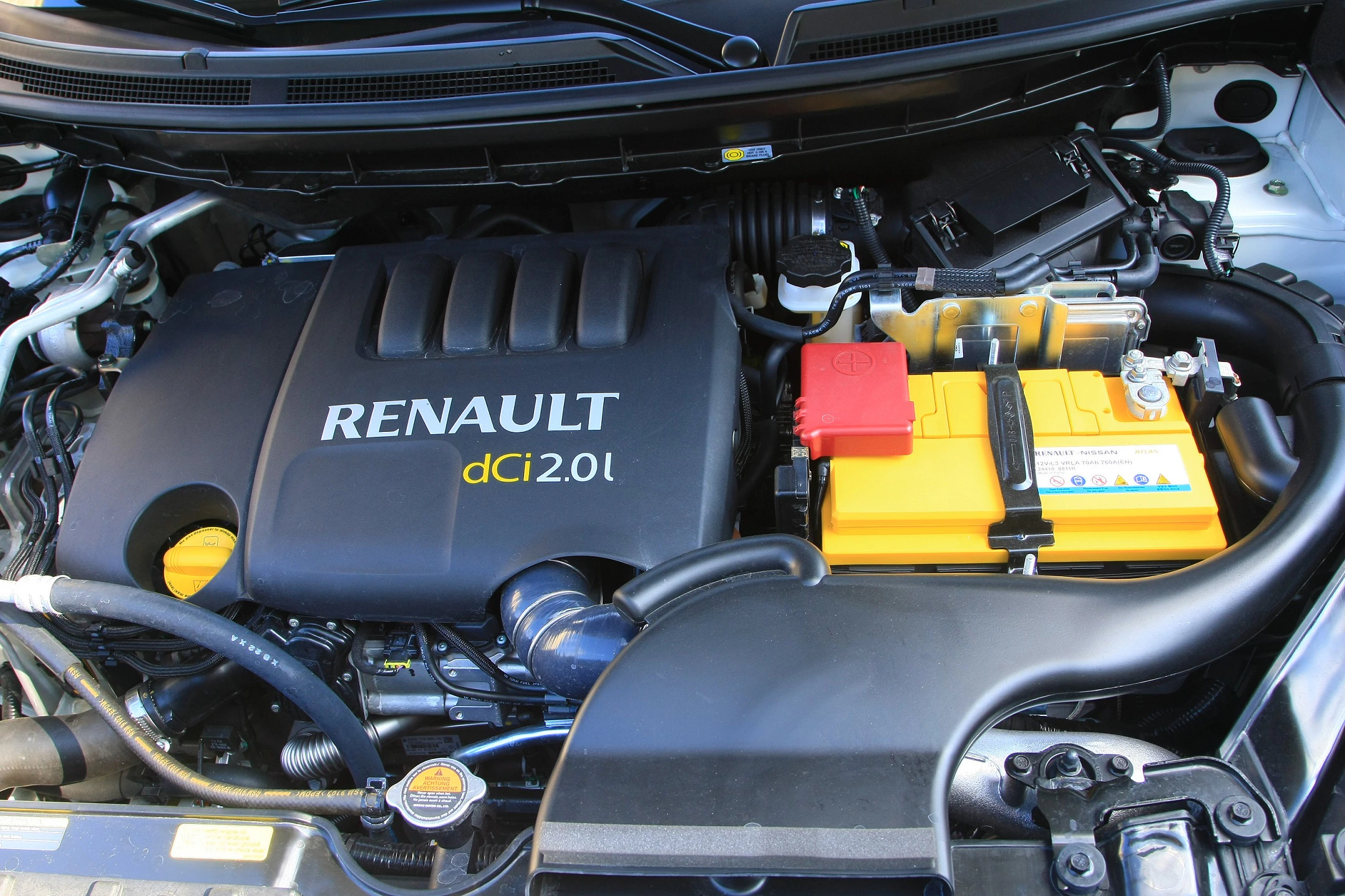 Nahaufnahme eines Renault-Motors mit gelber Batterie und der Aufschrift "dCi 2.0l" auf der Abdeckung.