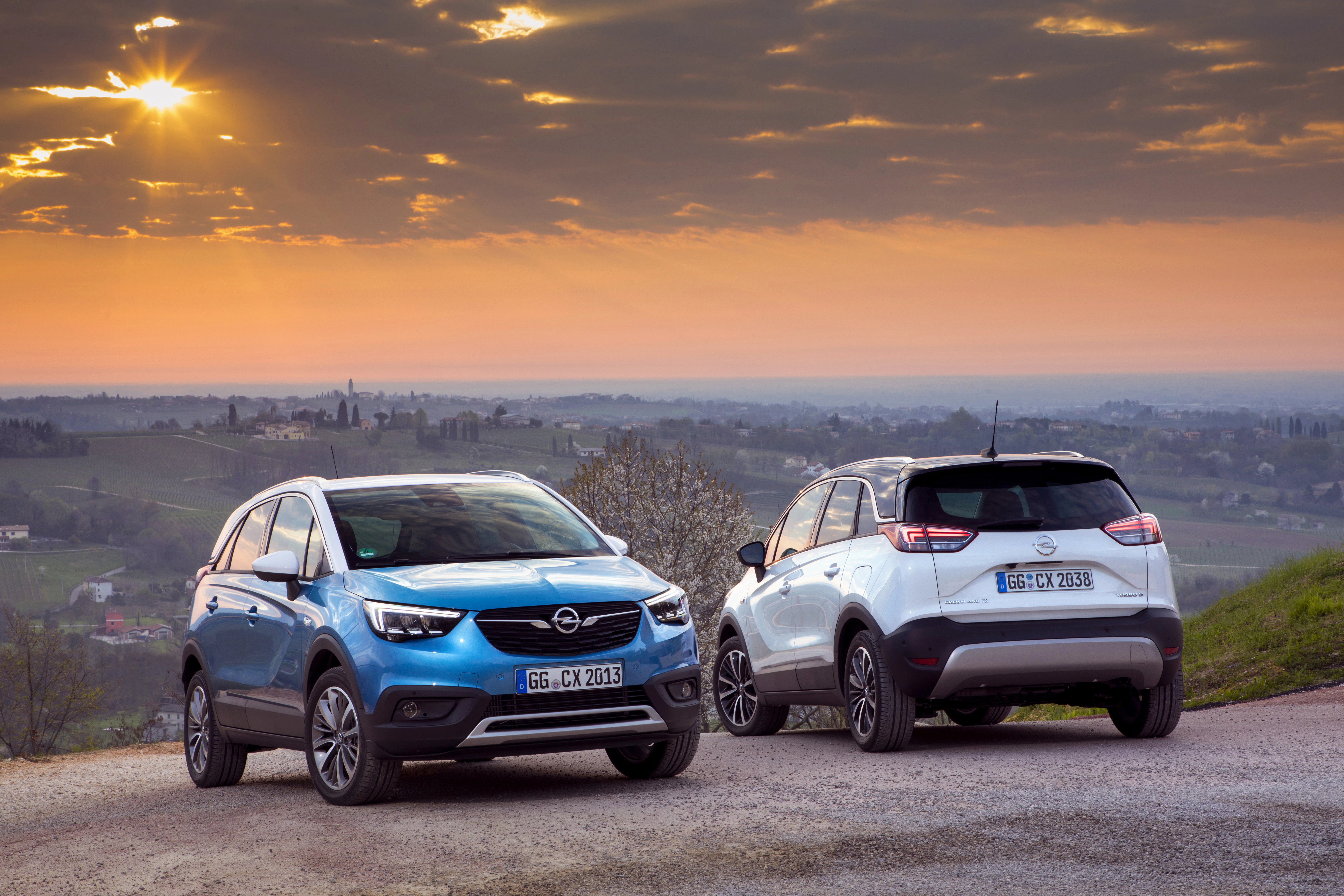 Zwei Opel-SUVs auf einer ländlichen Straße bei Sonnenuntergang, mit einer weiten Landschaft im Hintergrund.