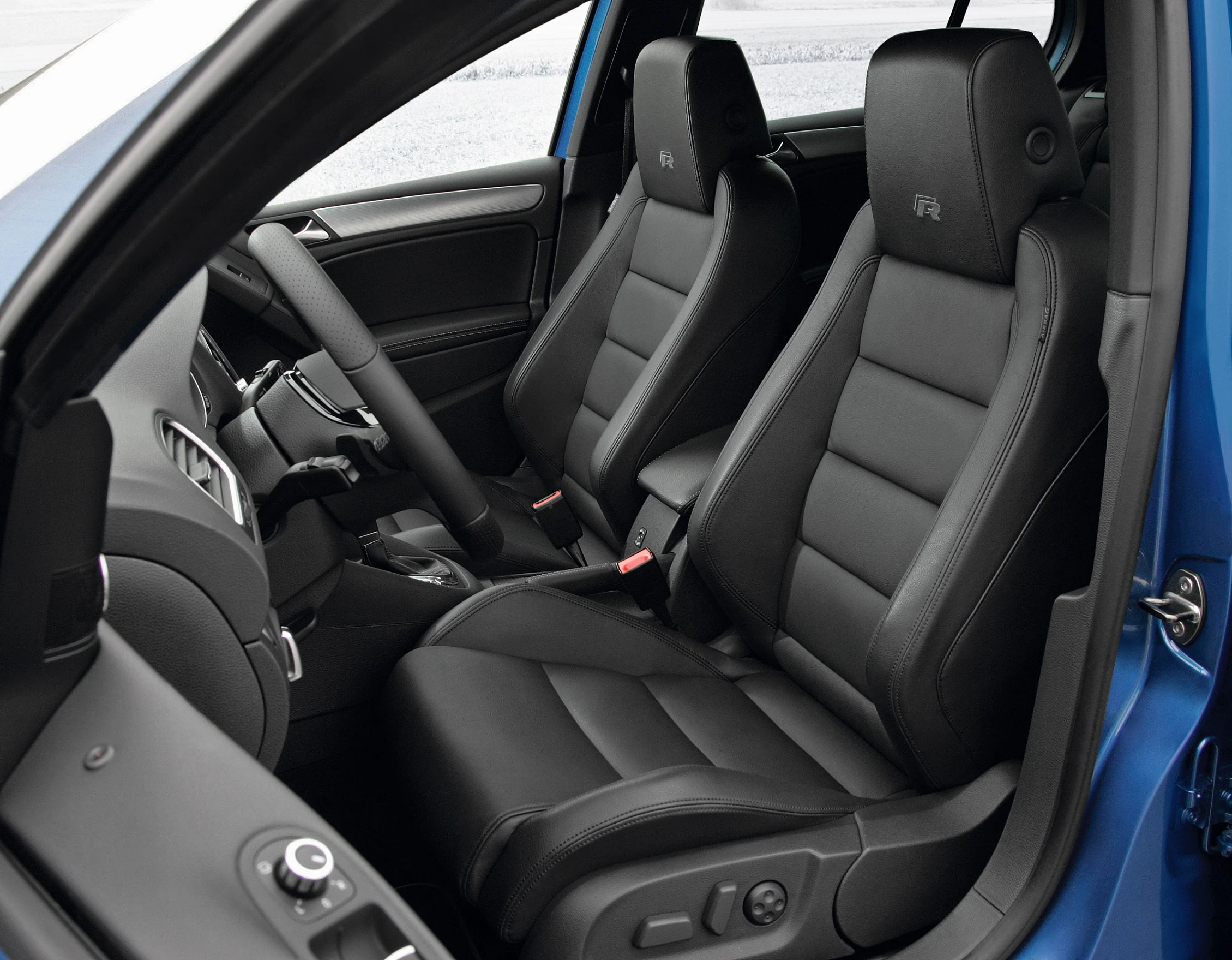 Innenraum eines Autos mit schwarzen Ledersitzen und modernem Armaturenbrett. Blaues Fahrzeugäußeres sichtbar durch die Tür.