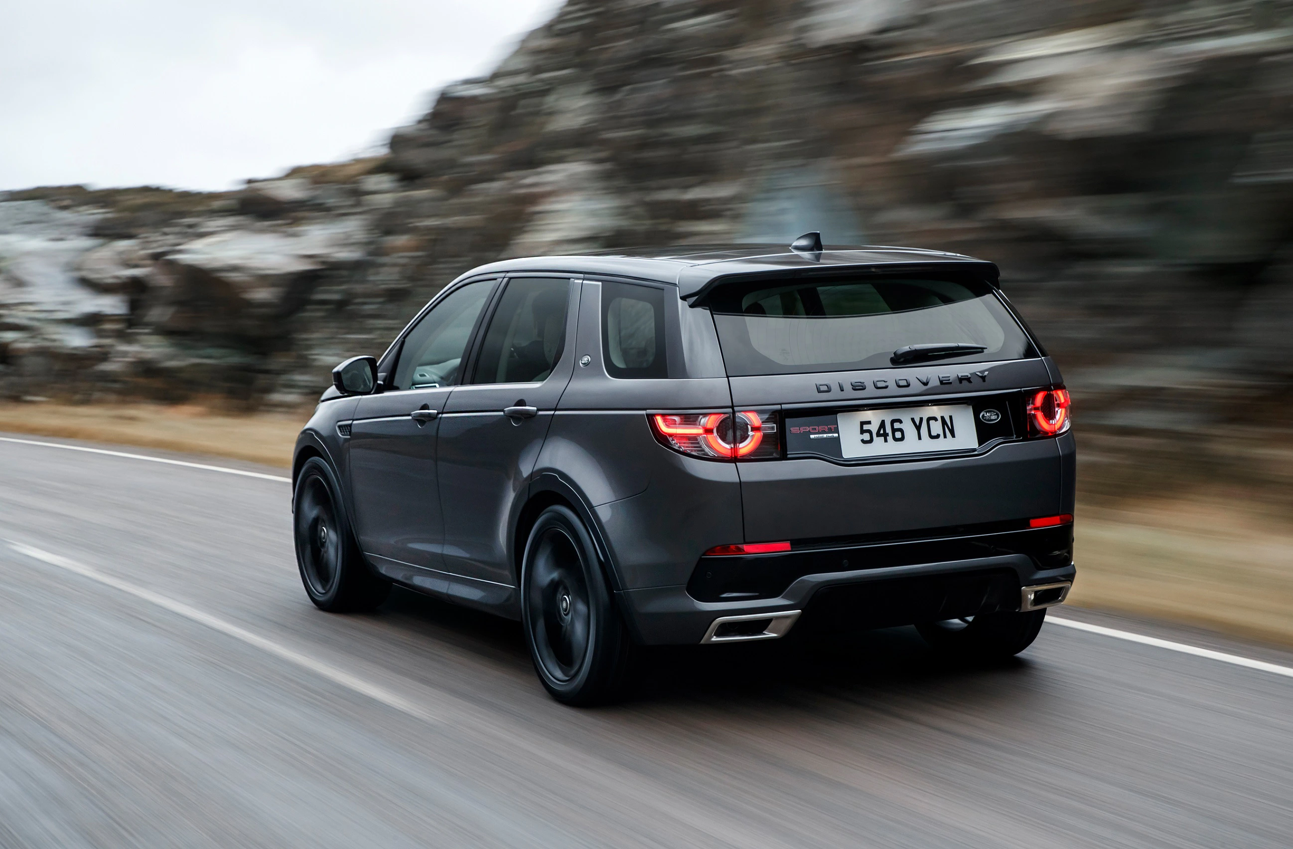 Grauer SUV fährt schnell auf einer Landstraße, Felsen im Hintergrund. Nummernschild mit der Aufschrift "546 YCN".