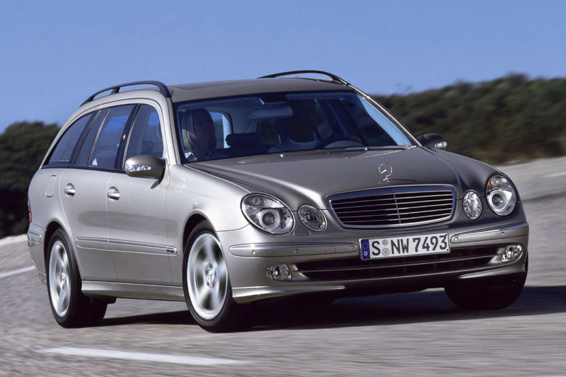 Silberner Kombi der Marke Mercedes-Benz fährt auf einer Straße. Das Fahrzeug hat eine Frontansicht mit markantem Kühlergrill.