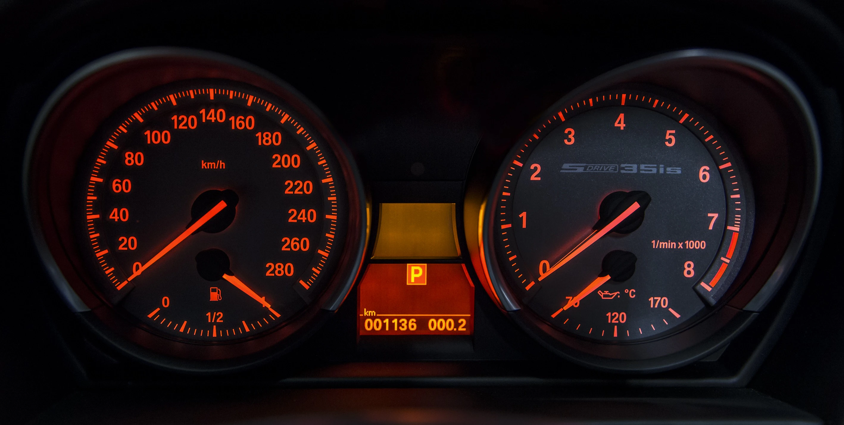 Armaturenbrett eines Autos mit Tachometer und Drehzahlmesser, zeigt 11 km/h an, Kilometerstand bei 1136, rote Hintergrundbeleuchtung.