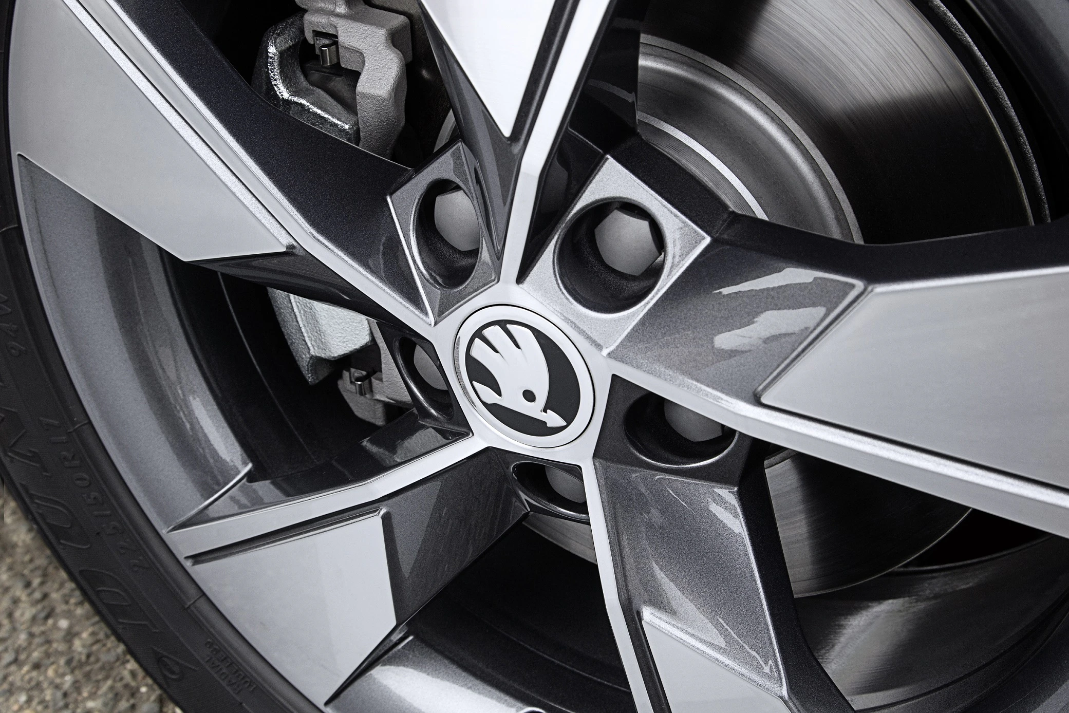 Großaufnahme einer silber-grauen Autoreifenfelge mit Skoda-Logo, glänzende Oberfläche, teilweise sichtbarer Bremsanlage im Hintergrund.